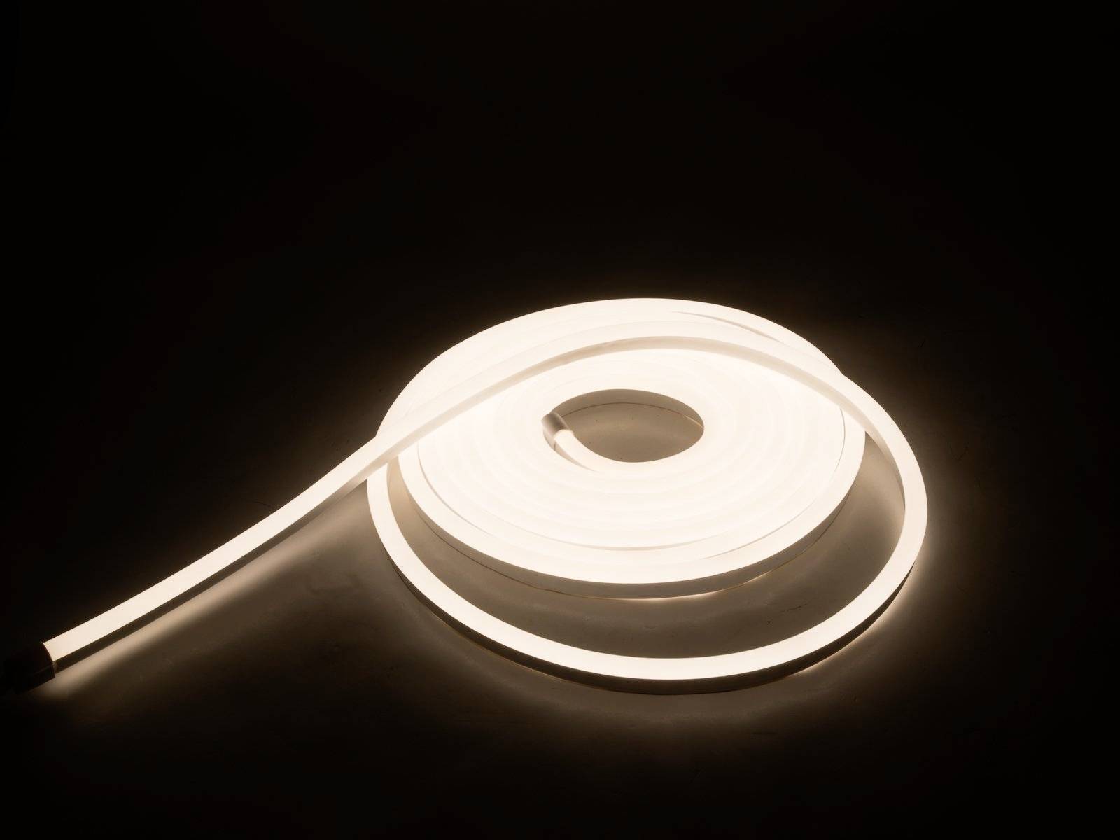 Ein zusammengerollter LED-Lichtstreifen leuchtet in warmem Weiß auf dunkelbraunem Hintergrund.