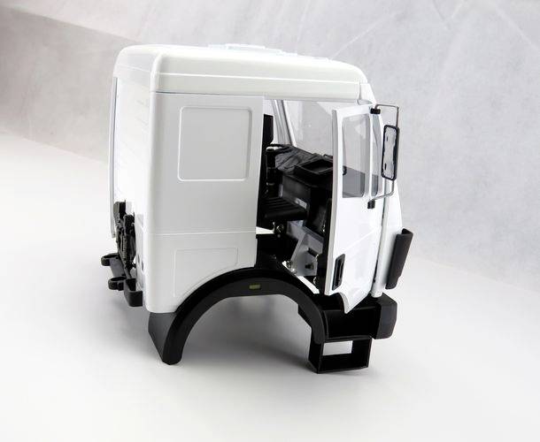 Miniaturmodell einer weißen Lkw-Fahrerkabine auf einer grauen Oberfläche, Türen geöffnet, zeigt Innenraumdetails des Fahrerbereichs.