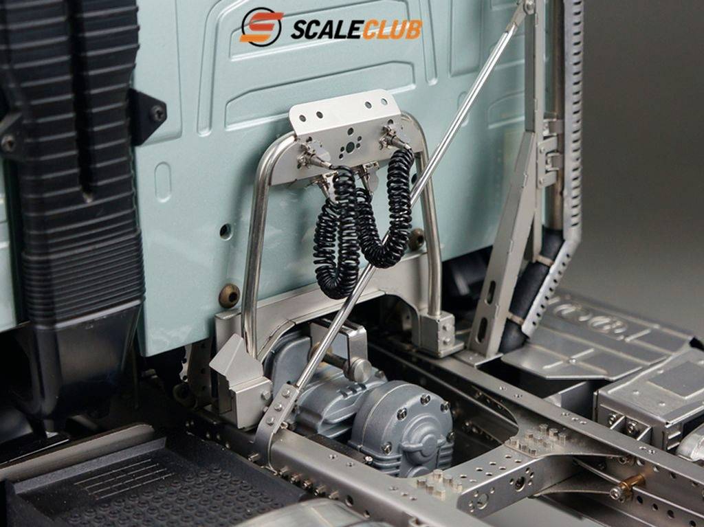 Modell eines LKW-Fahrgestells mit detaillierter Federung und Antrieb, vor einem hellblauen Hintergrund. Logo 'SCALE CLUB' oben links.