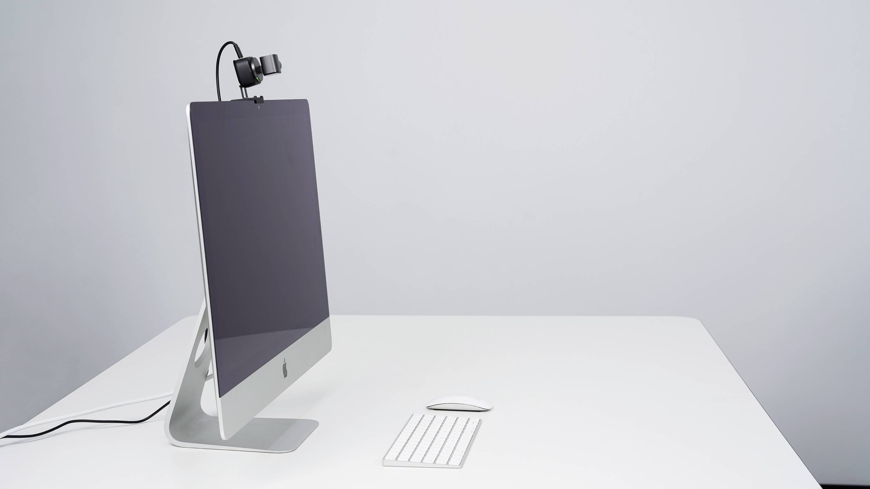 Ein moderner Computer mit Monitor, Tastatur und Maus auf einem weißen Tisch. Eine Webcam ist oben am Monitor angebracht.