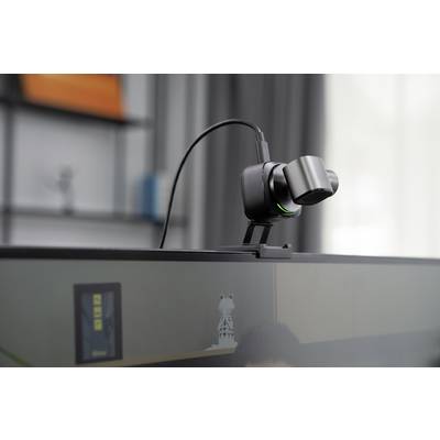 Eine Webcam ist oben auf einem Monitor montiert. Sie zeigt ein schwarzes Gehäuse mit einem grünen Licht und ist an ein Kabel angeschlossen.