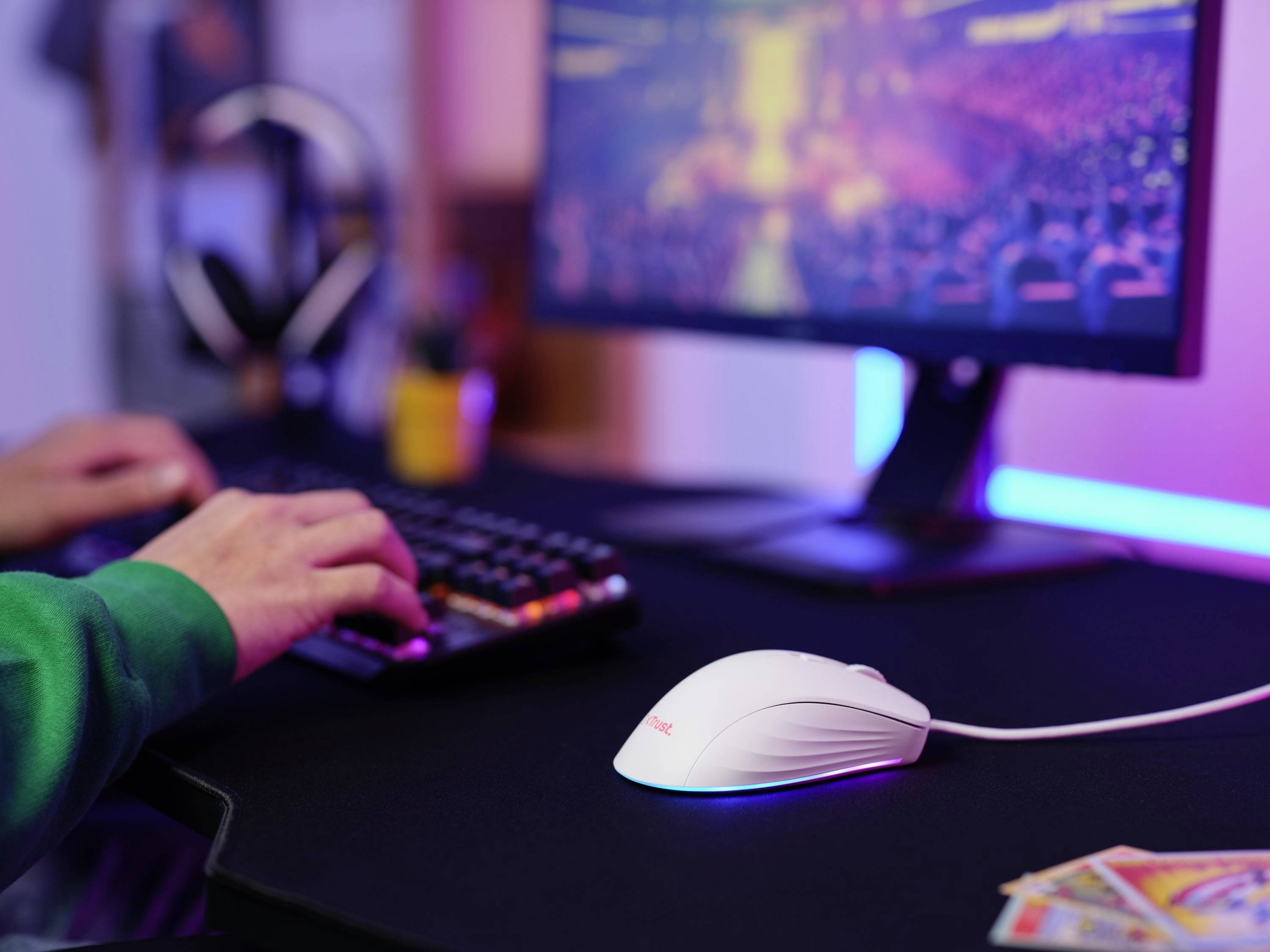 Eine Person sitzt an einem Schreibtisch und spielt ein Videospiel. Die Hände bedienen Tastatur und Maus. Ein Bildschirm zeigt eine verschwommene Spielszene.