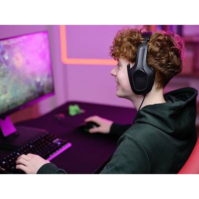 Eine Person mit Kopfhörern spielt an einem Computer, der von pinkem Licht beleuchtet wird.