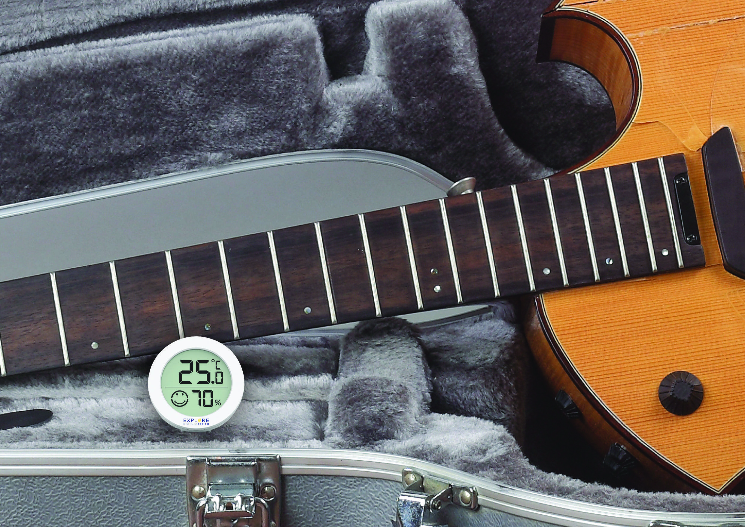 Eine Akustikgitarre liegt in einem offenen, mit Samt ausgekleideten Koffer. Ein Hygrometer zeigt 25,6 °C und 70 % Luftfeuchtigkeit an.