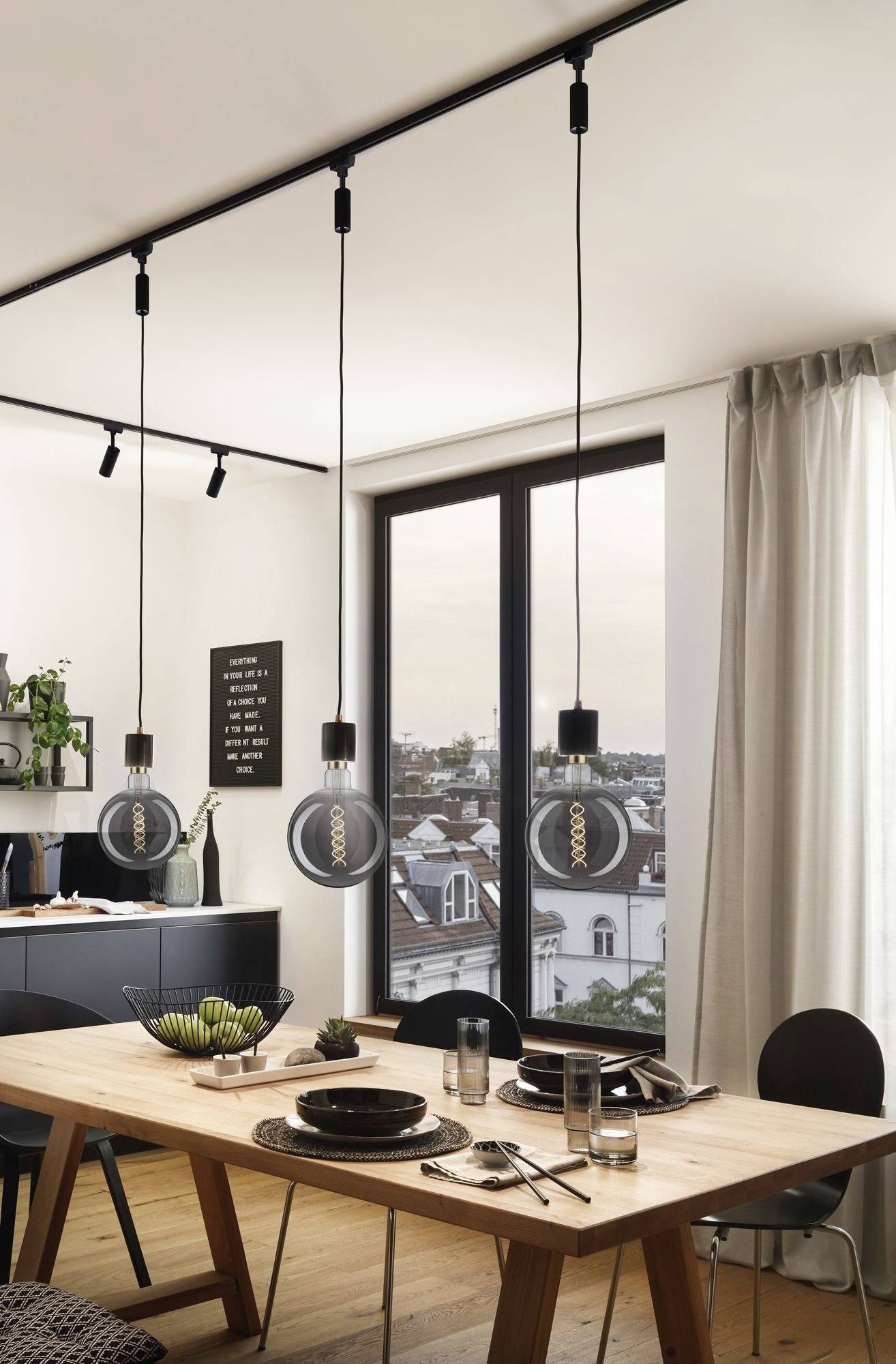 Ein modern eingerichtetes Esszimmer mit einem Holztisch, gedeckt mit Geschirr. Große Fenster bieten Ausblick auf eine Stadtlandschaft. Hängeleuchten beleuchten den Raum.