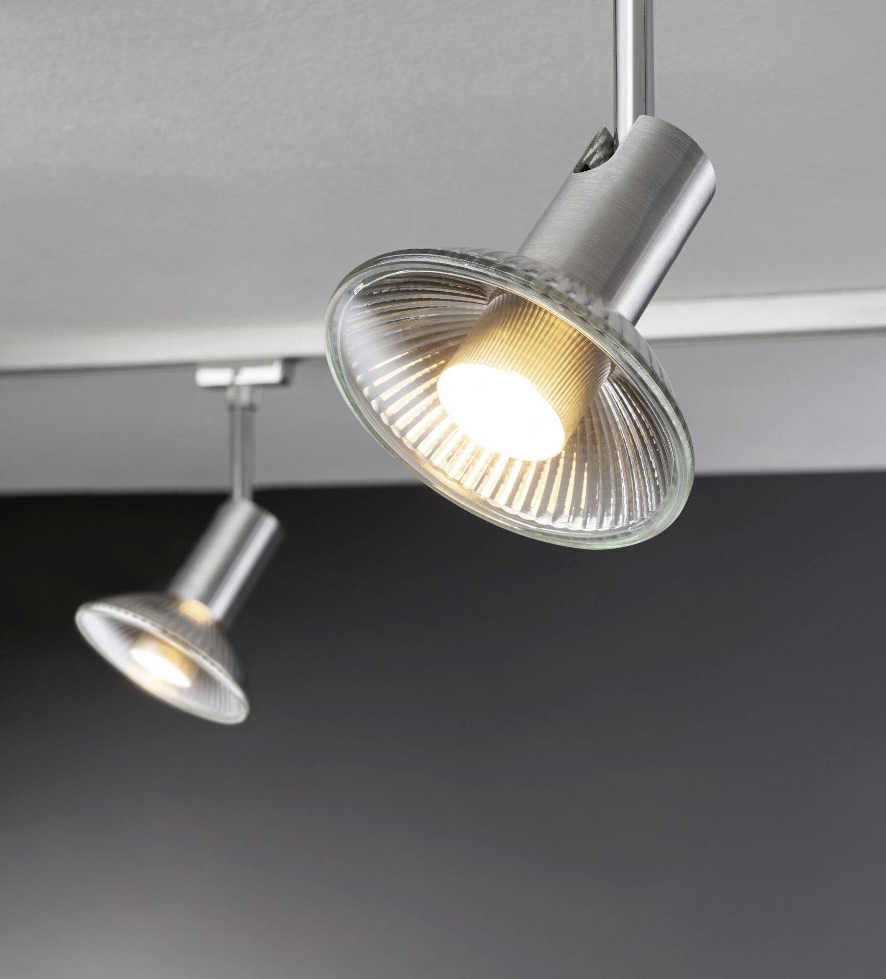 Zwei moderne Deckenstrahler mit Metalloptik, die warmes Licht ausstrahlen und gegen eine dunkle Wand gerichtet sind.