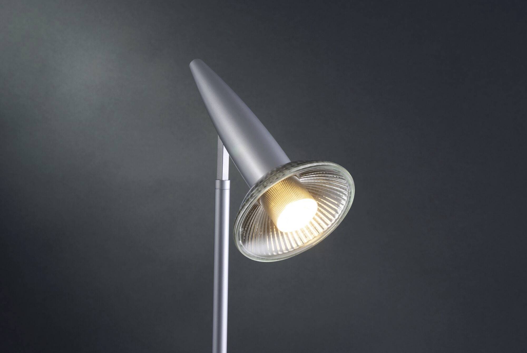 Eine moderne Stehlampe mit metallischem Korpus und geneigtem Lampenschirm, leuchtet in einem dunklen Raum.