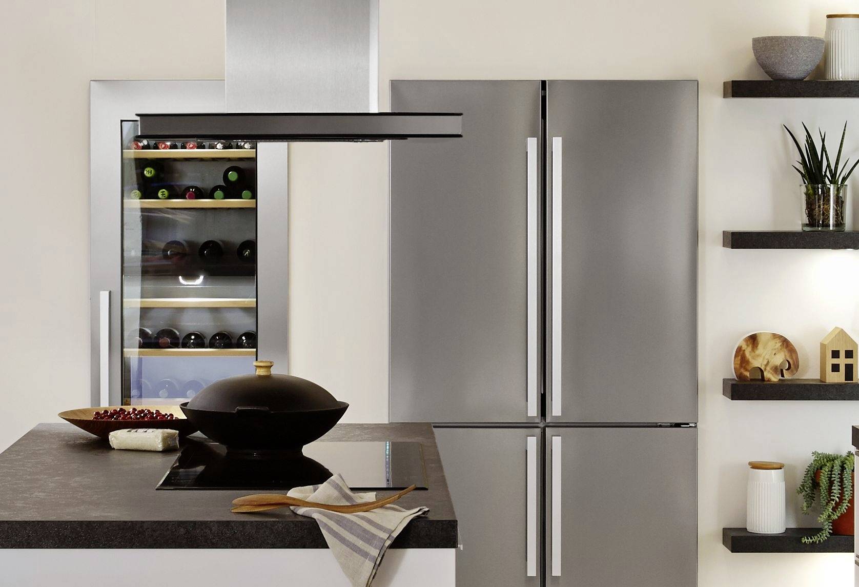 Moderne Küche mit grauen Schränken, Kühlschrank mit Doppeltür und eingebautem Weinkühler. Kochinsel mit schwarzem Topf im Vordergrund.