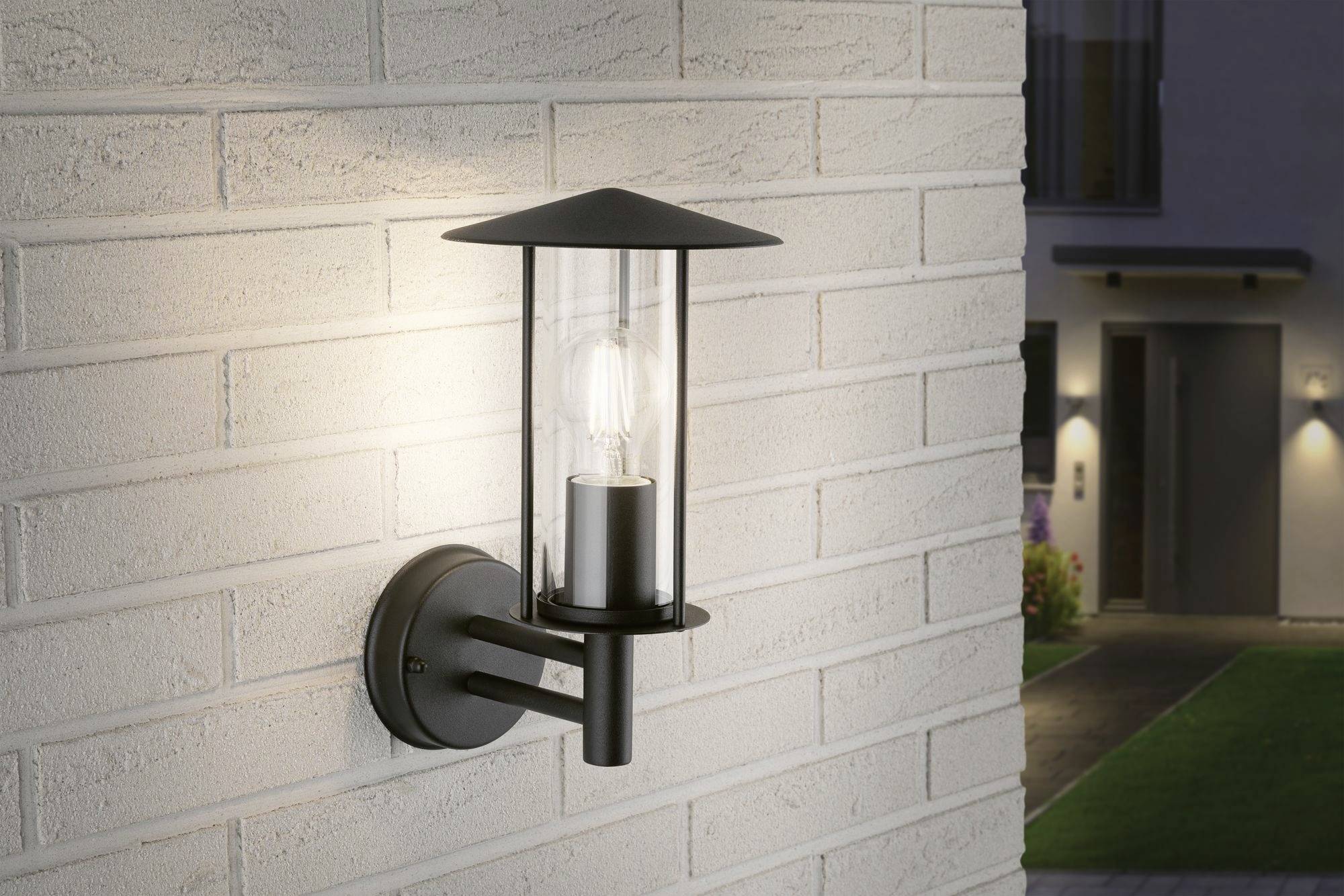 Außenwandlampe mit modernem Design an einer weißen Ziegelwand, beleuchtet den Eingang eines Hauses bei Nacht.