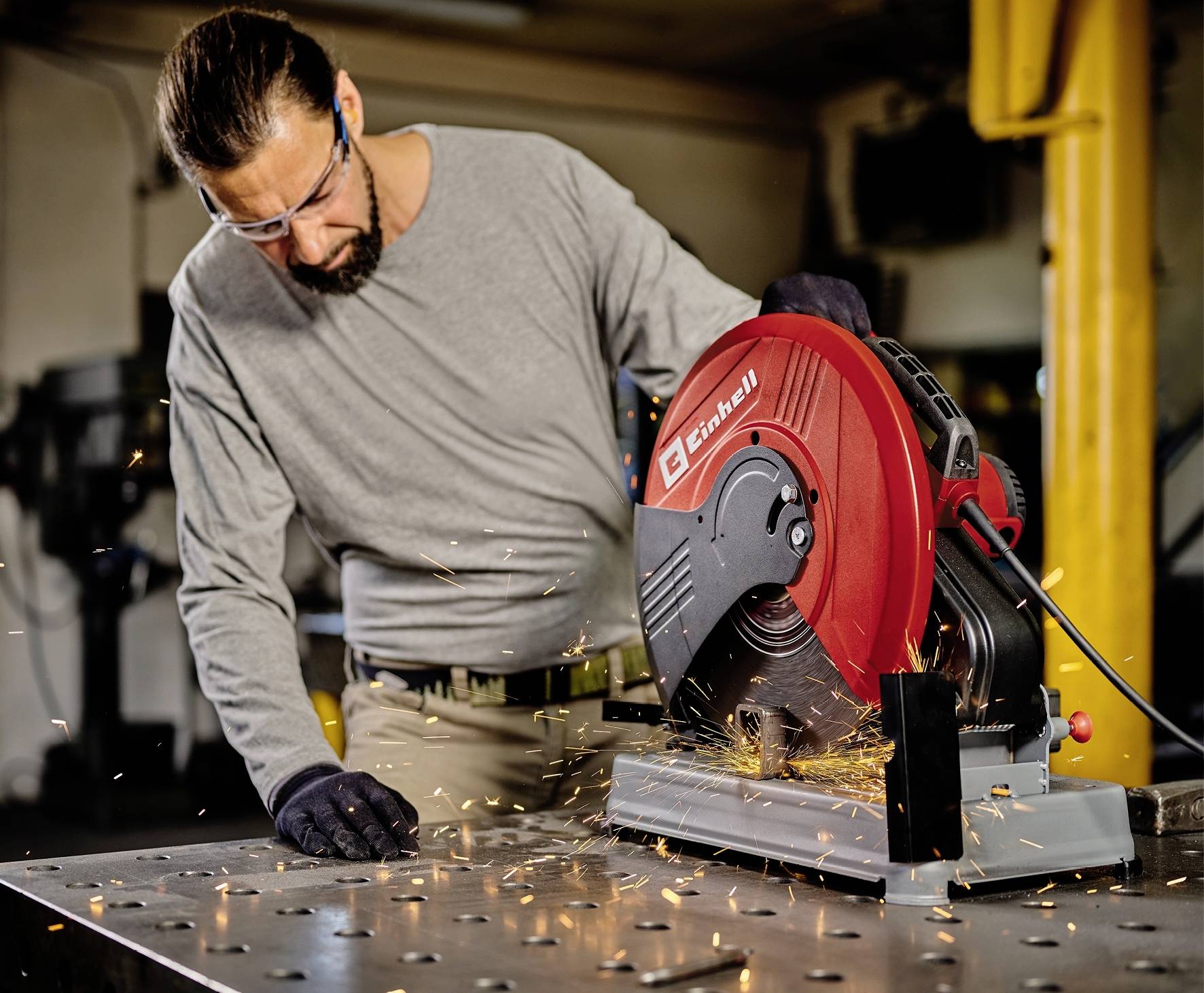 Ein Mann mit Schutzbrille bedient eine Trennsäge in einer Werkstatt. Funken fliegen, während er Metall schneidet.