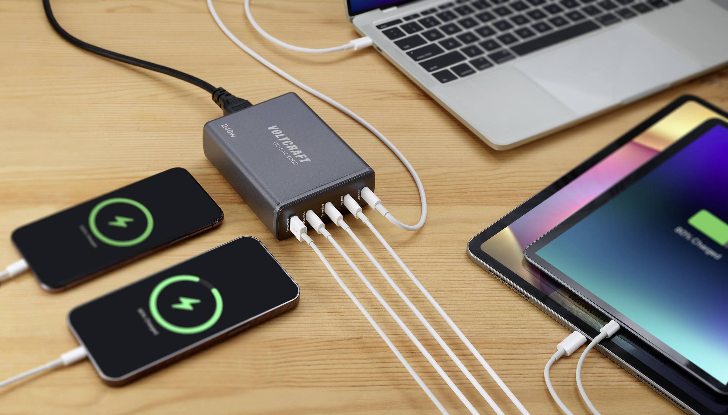Ein Mehrfach-USB-Ladegerät lädt gleichzeitig zwei Smartphones, ein Tablet und ein Laptop auf, alle Geräte zeigen Ladesymbole an.