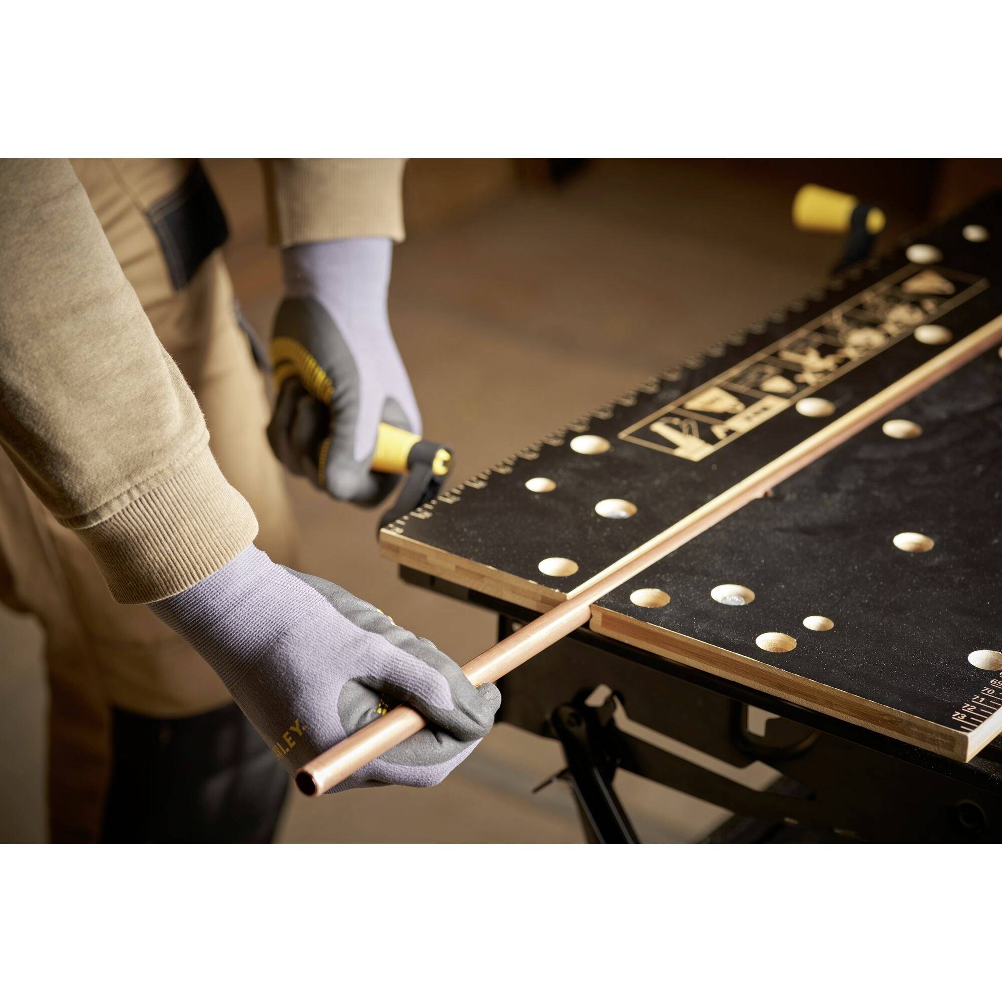 Eine Person arbeitet mit Handschuhen an einem Kupferrohr, das in einem Schraubstock auf einer Werkbank fixiert ist.