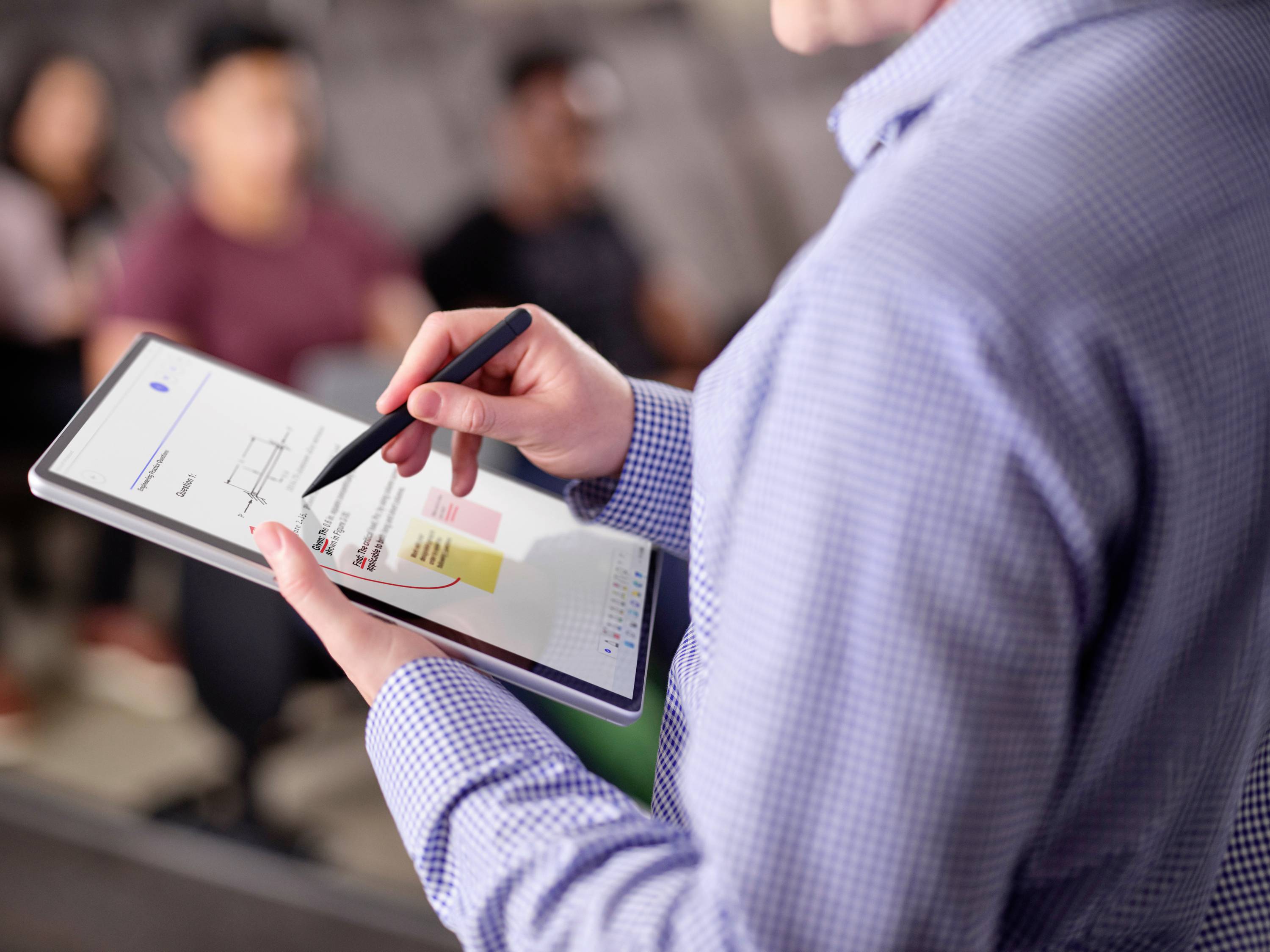 Person hält ein Tablet mit einem Diagramm, das markiert wird, während im Hintergrund unscharf eine Gruppe von Menschen sitzt.