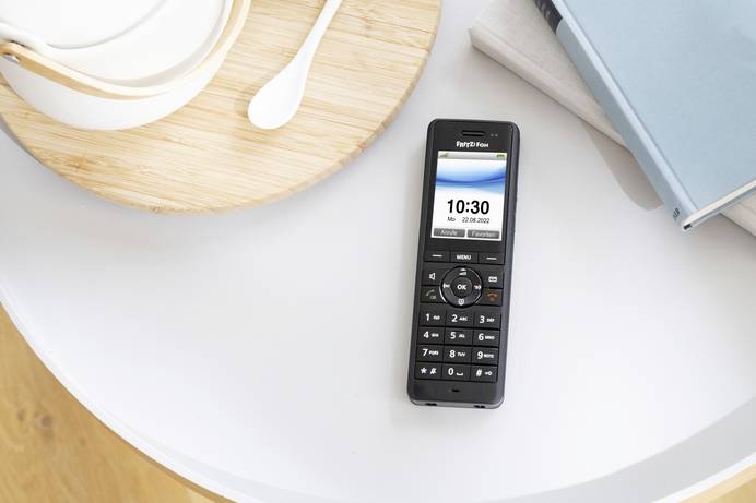 Der Mobilteil eines VoIP-Telefons liegt auf einem runden Tisch. Daneben finden sich Bücher und ein Tablett mitsamt Kanne und Löffel.