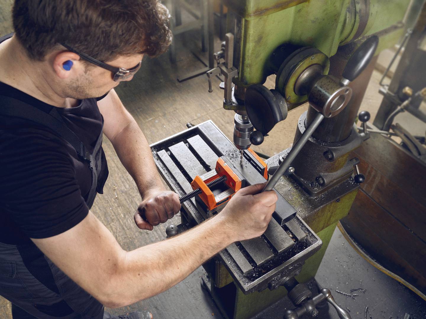 Ein Mann arbeitet an einer Fräsmaschine in einer Werkstatt. Er trägt Gehörschutz und benutzt einen Schraubenschlüssel zum Einstellen der Maschine.