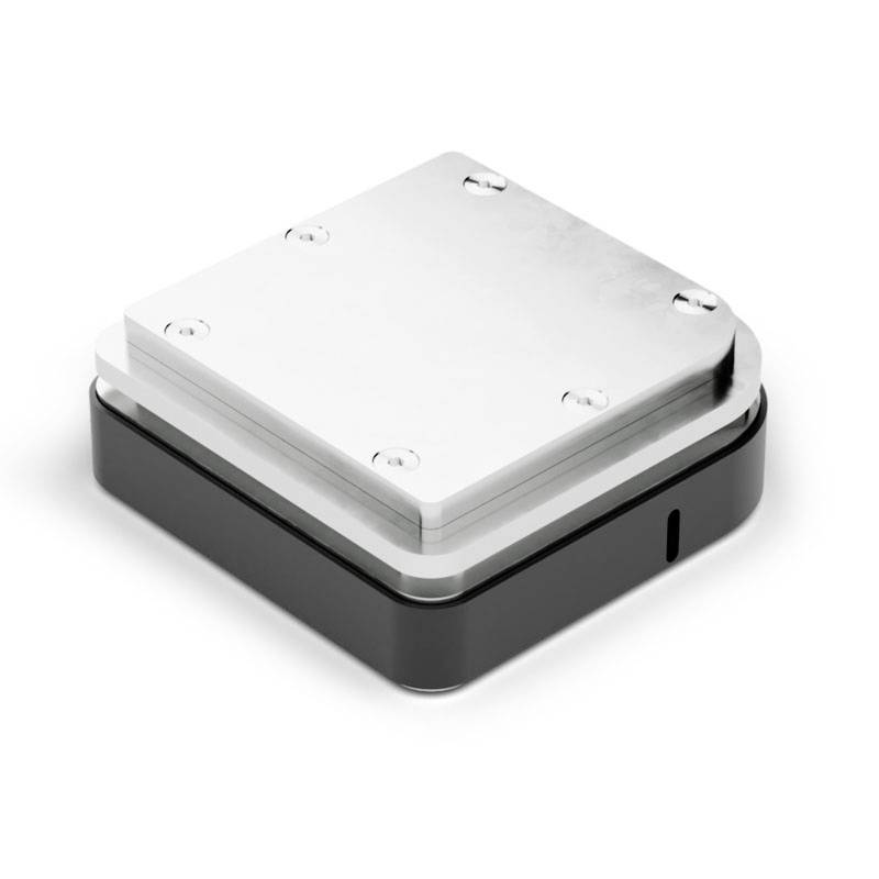 Ein viereckiges Metallgerät mit Schrauben an den Ecken, auf einem schwarzen Gehäuse montiert. Es könnte ein technisches Bauteil sein.