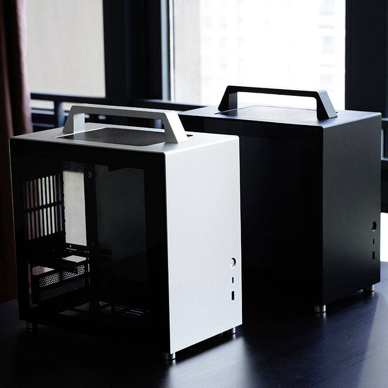 Zwei einfache, moderne Computergehäuse aus Metall und Glas, eines weiß, eines schwarz, stehen auf einem Tisch nah am Fenster.