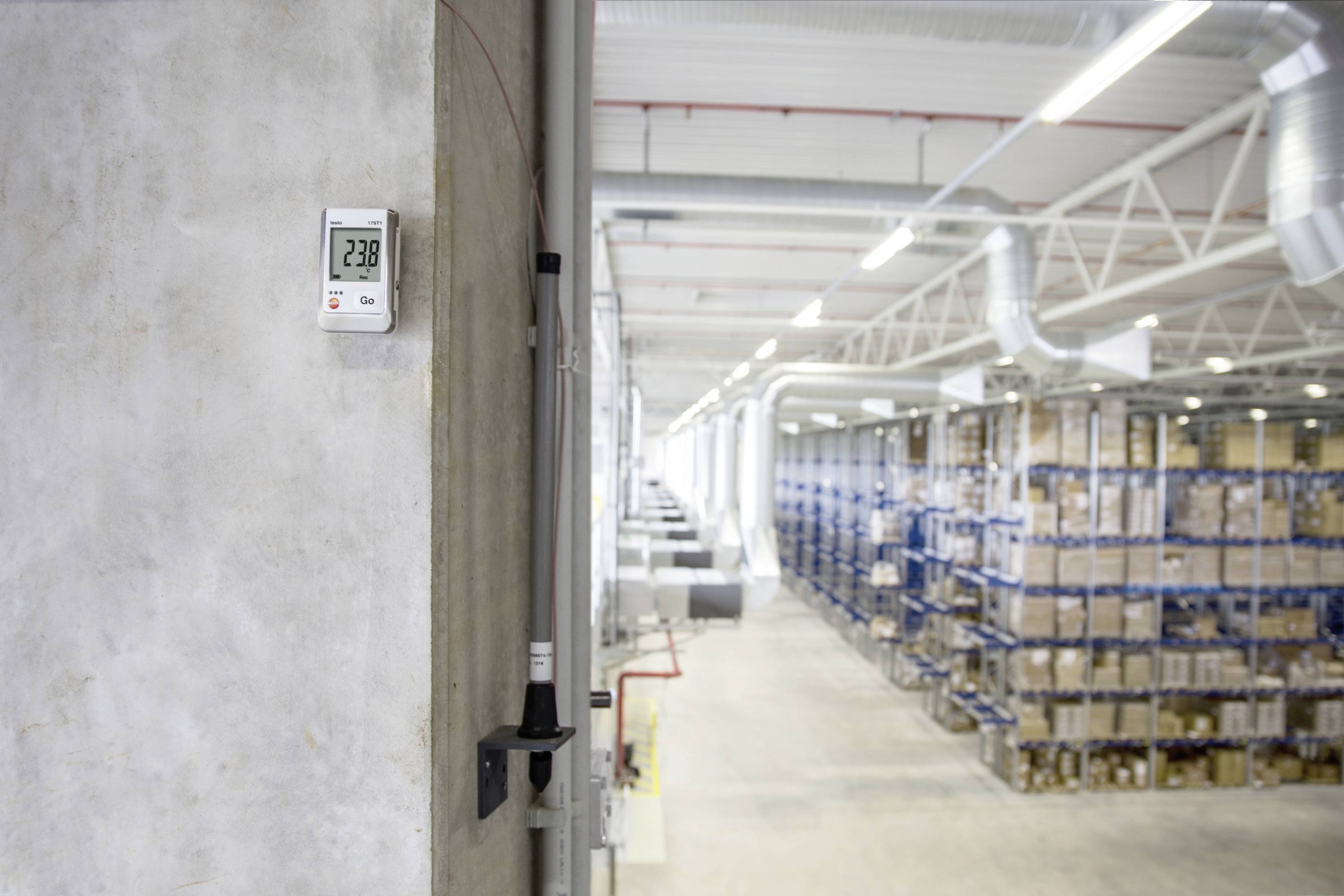 Eine Lagerhalle mit umfangreichen Regalen voller Kartons. Ein Temperaturmessgerät zeigt an der Wand 23,8 Grad Celsius an.