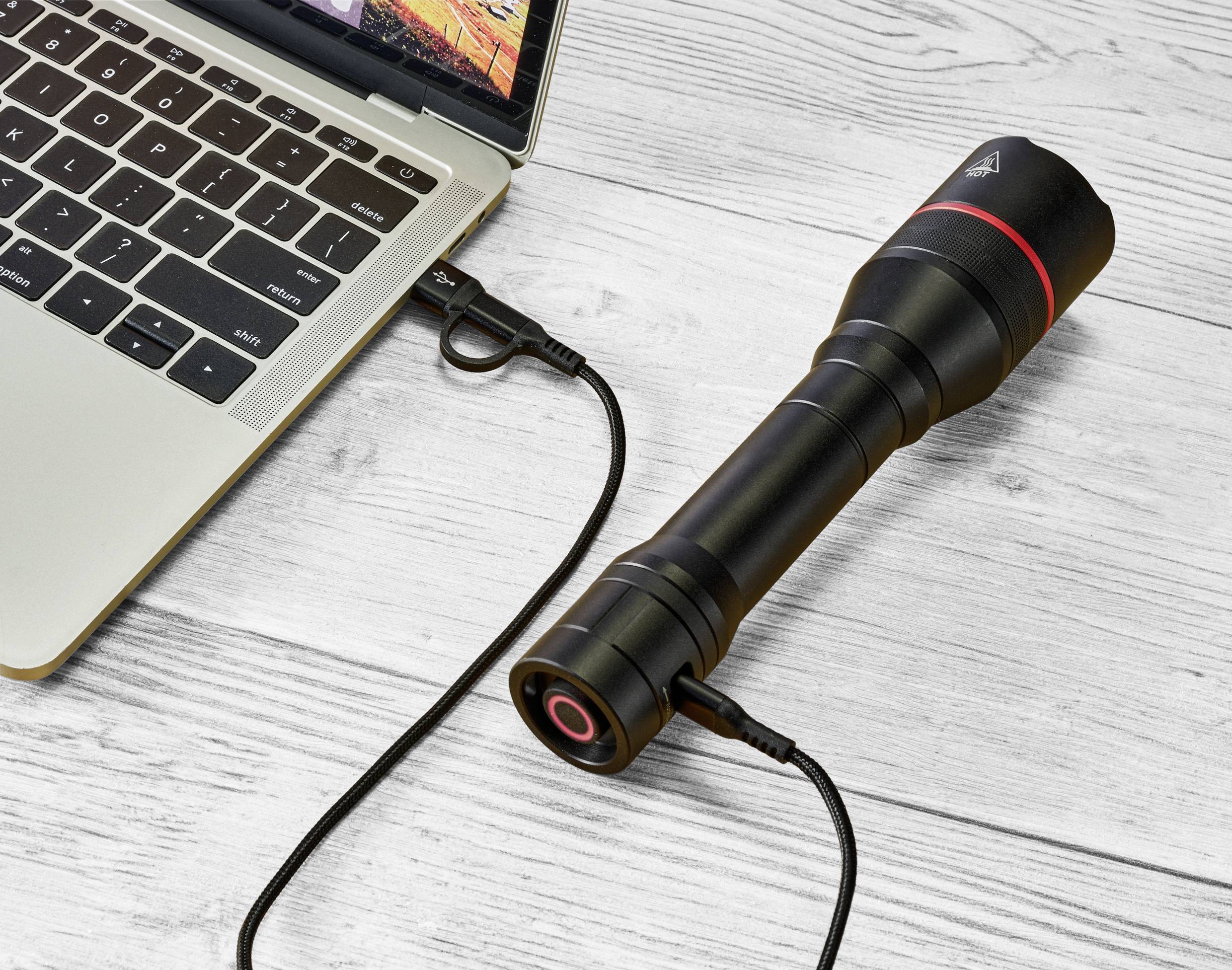 Eine Taschenlampe ist über ein USB-Kabel mit einem Laptop verbunden, zeigt eine Lade- oder Datenübertragungsfunktion an.