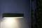 Eine rechteckige, moderne Lampe strahlt warmes Licht auf eine Wand.