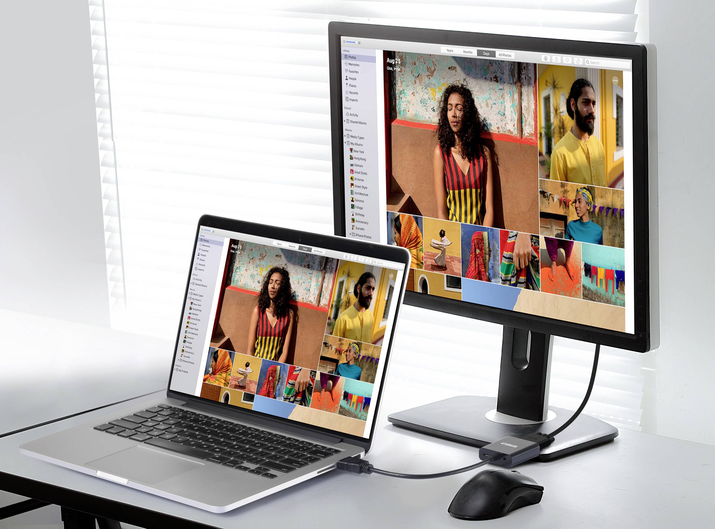 Ein Laptop und ein Monitor zeigen dasselbe Bild eines Videokonferenzscreens mit farbenfrohem Hintergrund in einem hellen Raum.