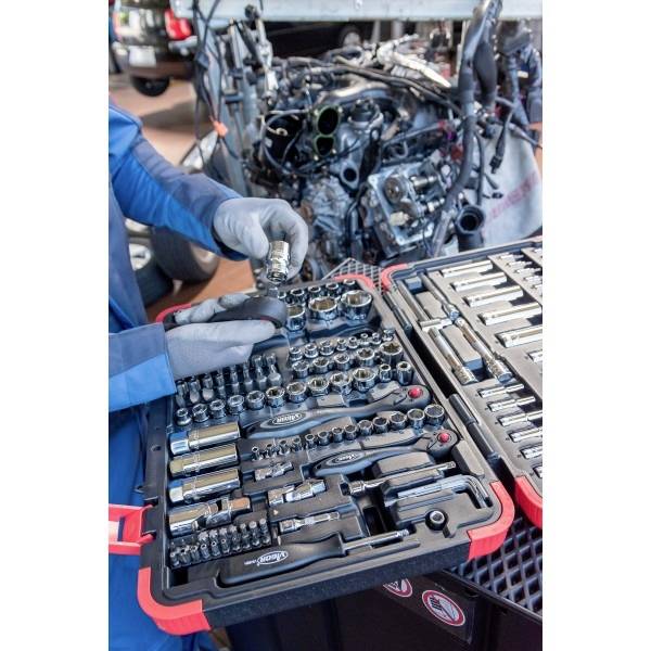 Ein Mechaniker wählt ein Werkzeug aus einem Steckschlüsselsatz in der Nähe eines Automotors aus, der gerade repariert wird, was laufende Fahrzeugwartungsarbeiten zeigt.