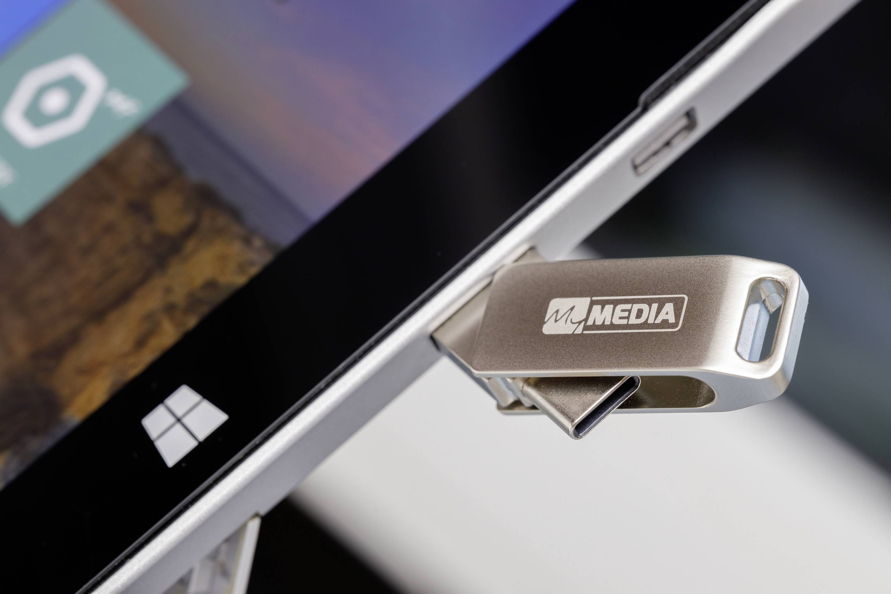 Ein USB-Stick mit 'Media' Logo steckt in einem Laptop. Das Laptopbildschirm zeigt Teile eines App-Symbols und Windows-Logo.