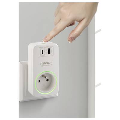 Eine Hand greift, um auf einen Knopf an einer weißen Steckdose mit USB-Anschlüssen zu drücken. Ein grüner Lichtkranz umgibt die Steckdose und zeigt an, dass sie eingeschaltet ist.