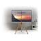 Moderner Flatscreen-Fernseher auf einem Holzständer mit einem Sonnenuntergang auf dem Bildschirm, platziert vor einer grauen Wand.