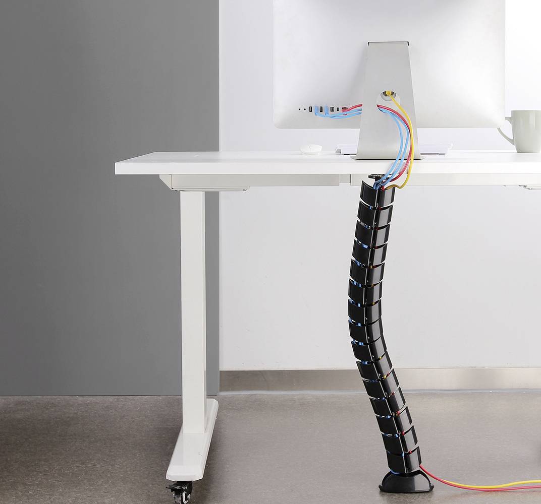 Ein Schreibtisch mit Kabelmanagementsystem, das geordnete Kabel hinter dem Tisch bündelt. Der Bildschirm ist auf dem Tisch platziert.