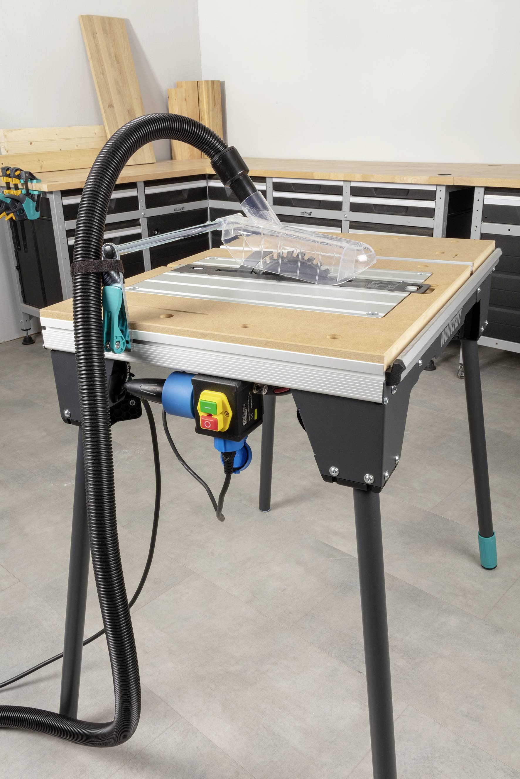 'Werkbank mit Tischsäge, Schlauch und Zubehör in Werkstattraum.'