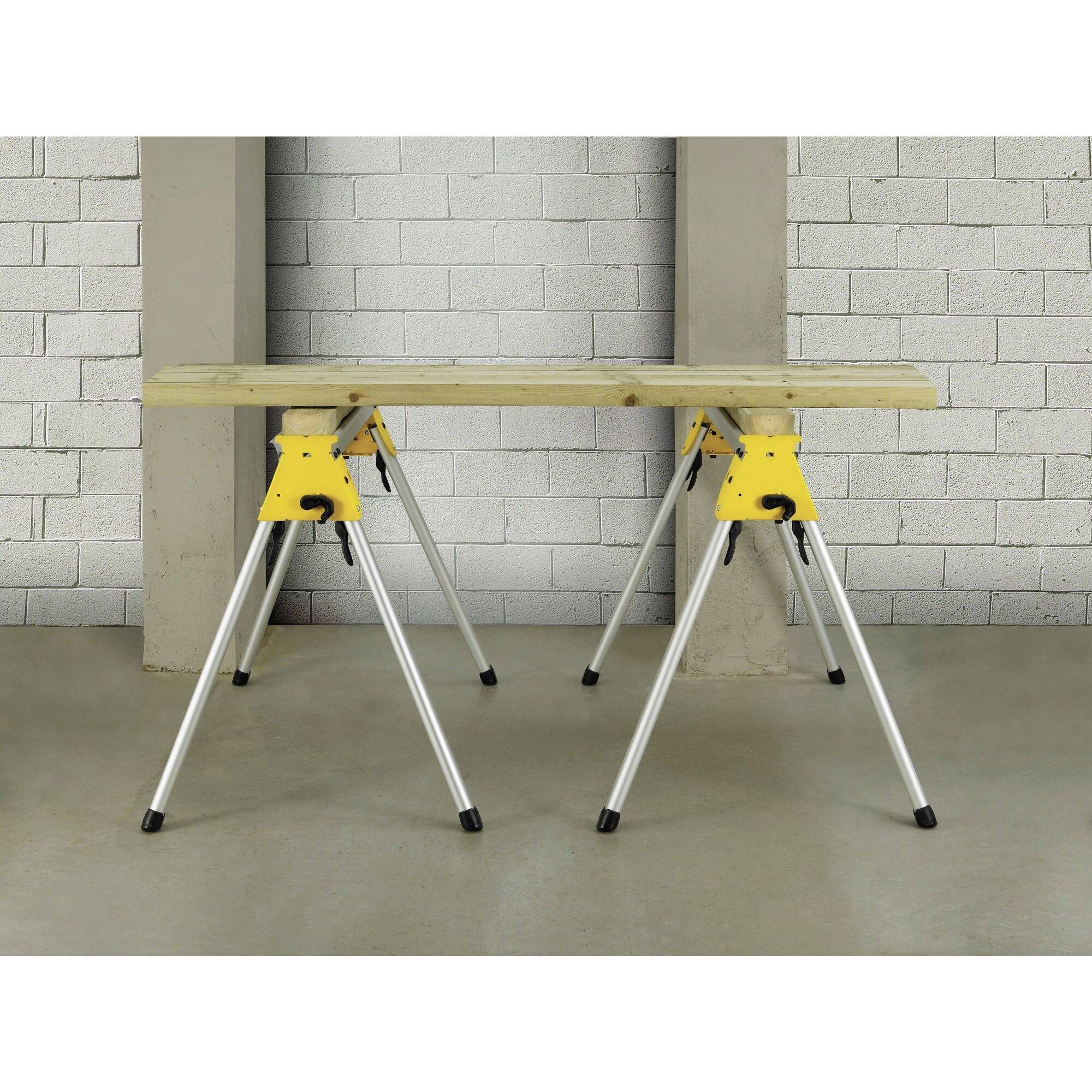 Ein stabiler Arbeitstisch auf zwei gelben Klappböcken vor einer grauen Ziegelwand. Ideal für Bau- oder Handwerksarbeiten.