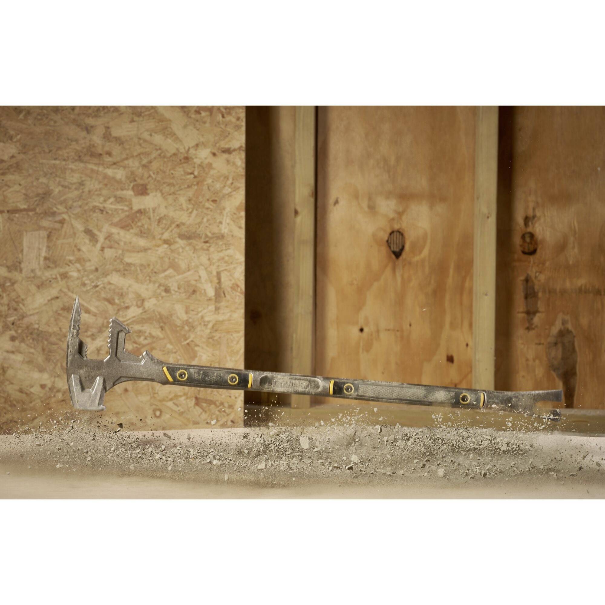 Ein Multifunktionswerkzeug mit Hammer- und Brechfunktion liegt auf einer Baustelle, umgeben von Betonstaub, vor einer Holzwand.