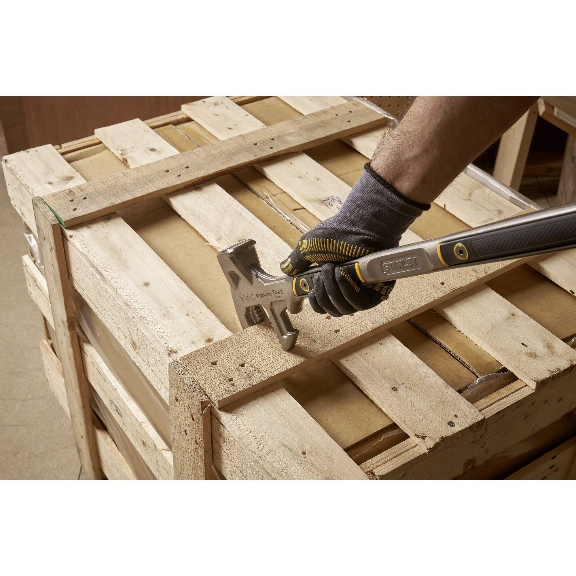 Eine Person mit Handschuhen verwendet einen Hammer, um ein Nagel aus einer Holzpalette zu entfernen.