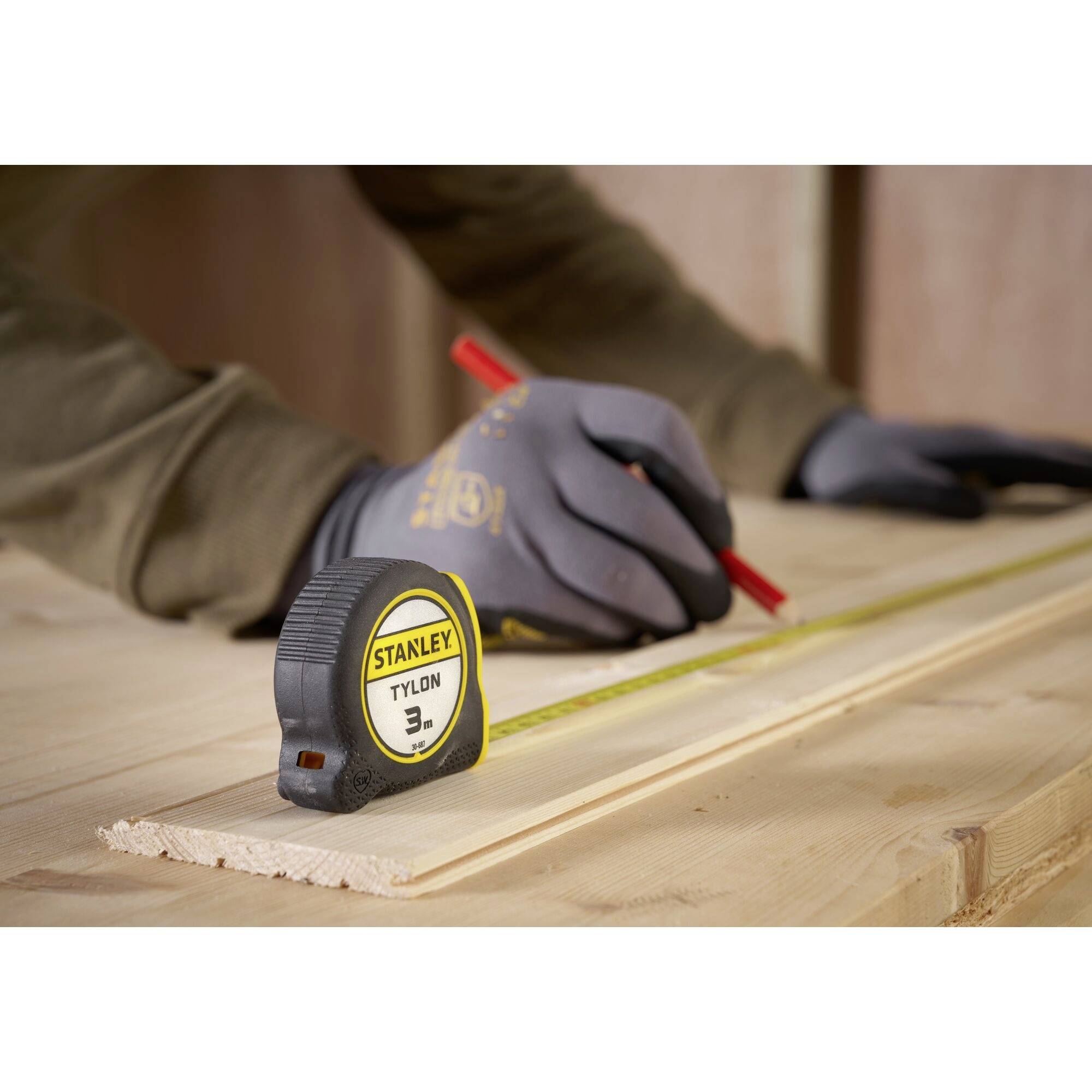 Eine Person misst ein Holzbrett mit einem Maßband und markiert es mit einem roten Stift.