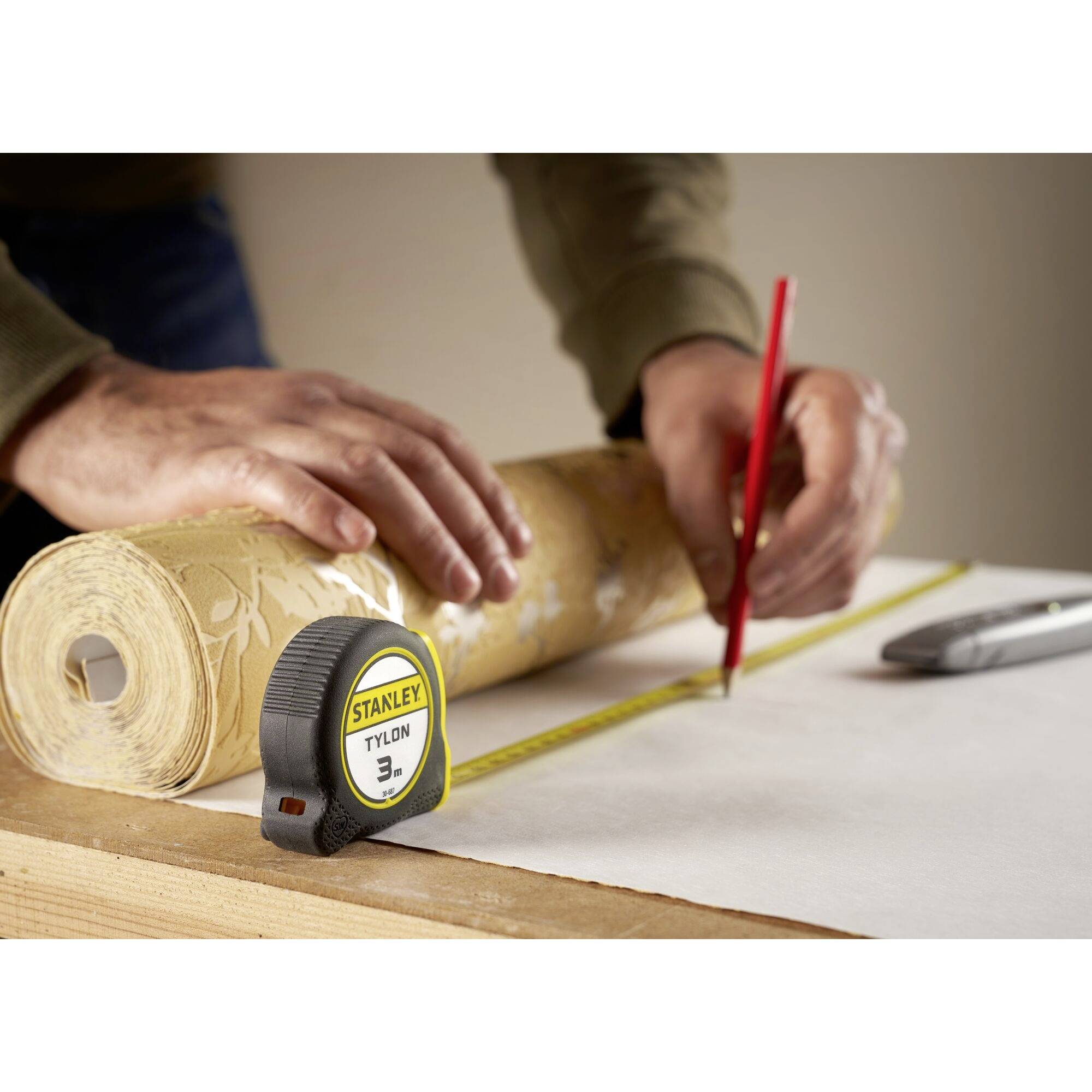 Eine Person zeichnet eine Linie auf Papier mit einem roten Bleistift und verwendet ein Maßband zur genauen Messung.