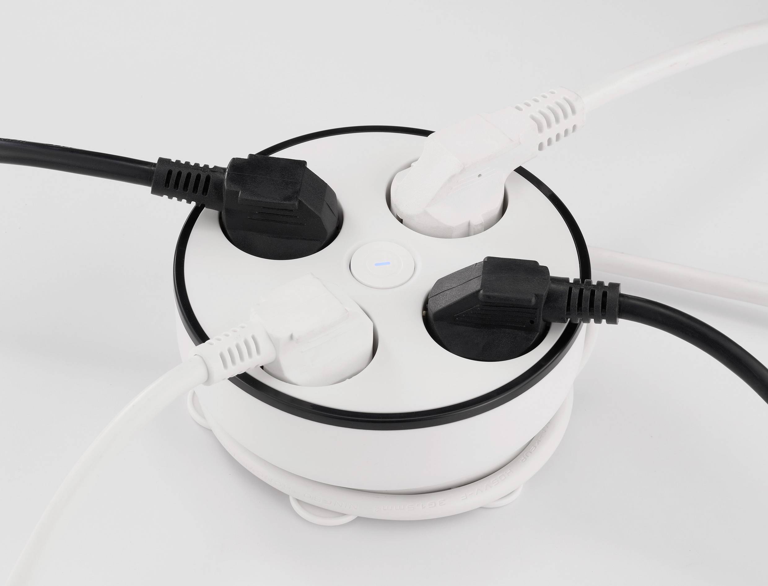 Vier eingesteckte Kabel in einer runden weißen Steckdosenleiste auf weißem Hintergrund.