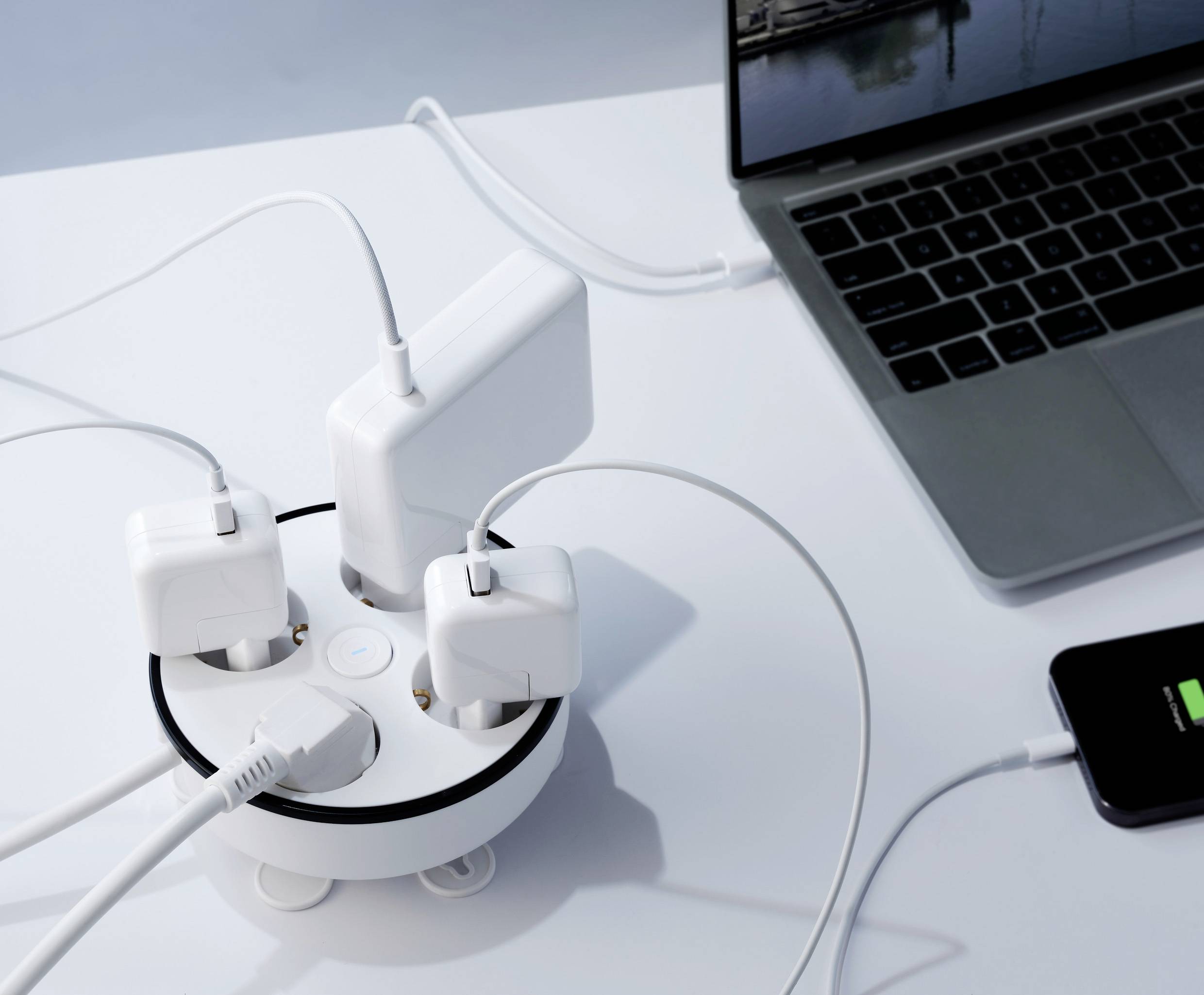 Ein Laptop und ein Smartphone sind mit einem runden Mehrfachstecker verbunden, an dem mehrere Ladegeräte angeschlossen sind.