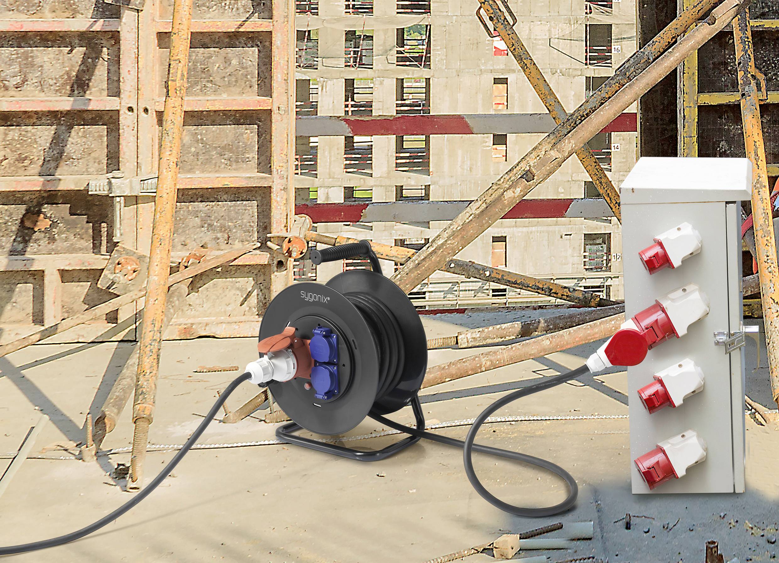 Baugerüst und Steckdosenverteiler auf Baustelle, verbunden mit einer Kabeltrommel. Hintergrund zeigt unvollendetes Gebäude.