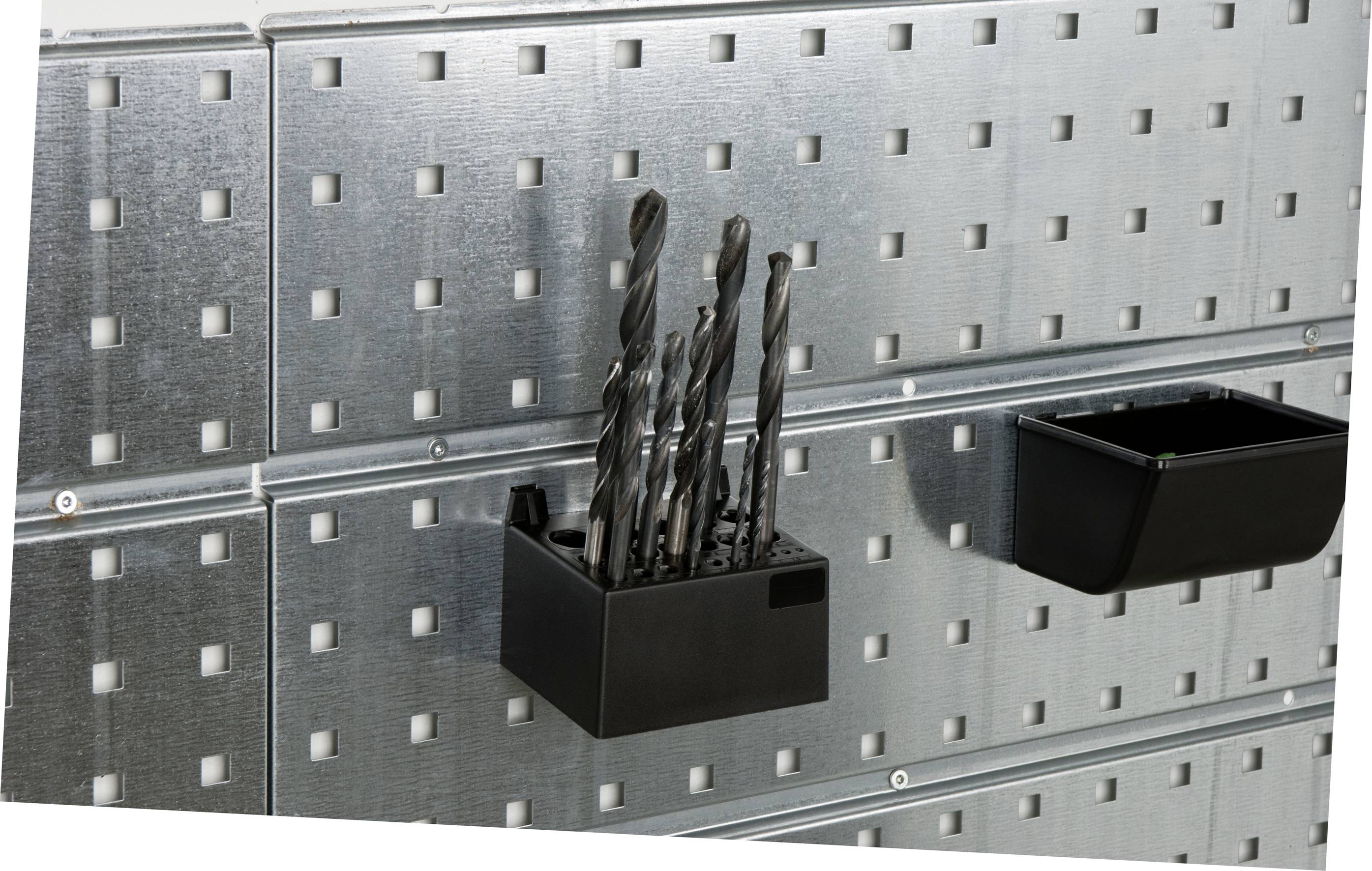 Ein Metallregal mit Bohrern in einem schwarzen Halter, daneben ein leerer Behälter. Der Hintergrund ist eine gelochte Metallwand.