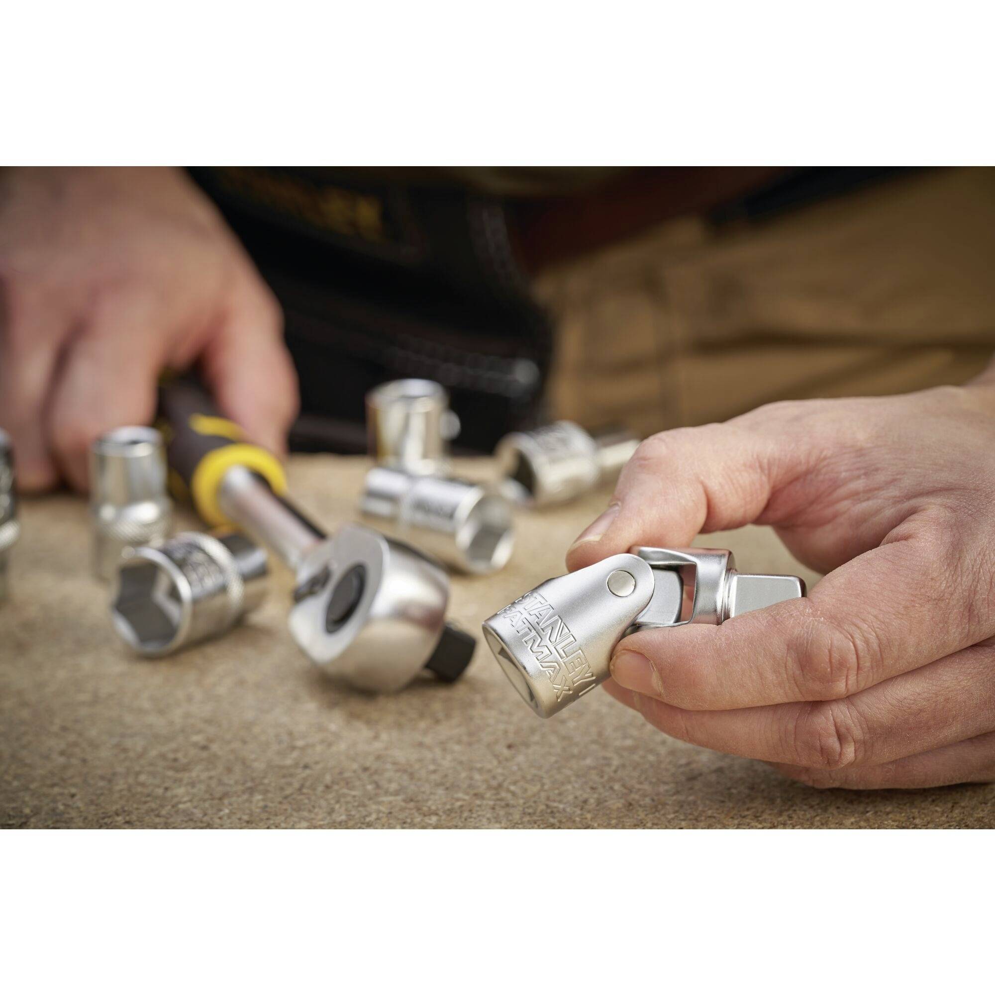 Eine Person hält ein Metallschraubwerkzeug in der Hand, während verschiedene Werkzeuge auf einem Tisch liegen. Fokus auf das Werkzeug.