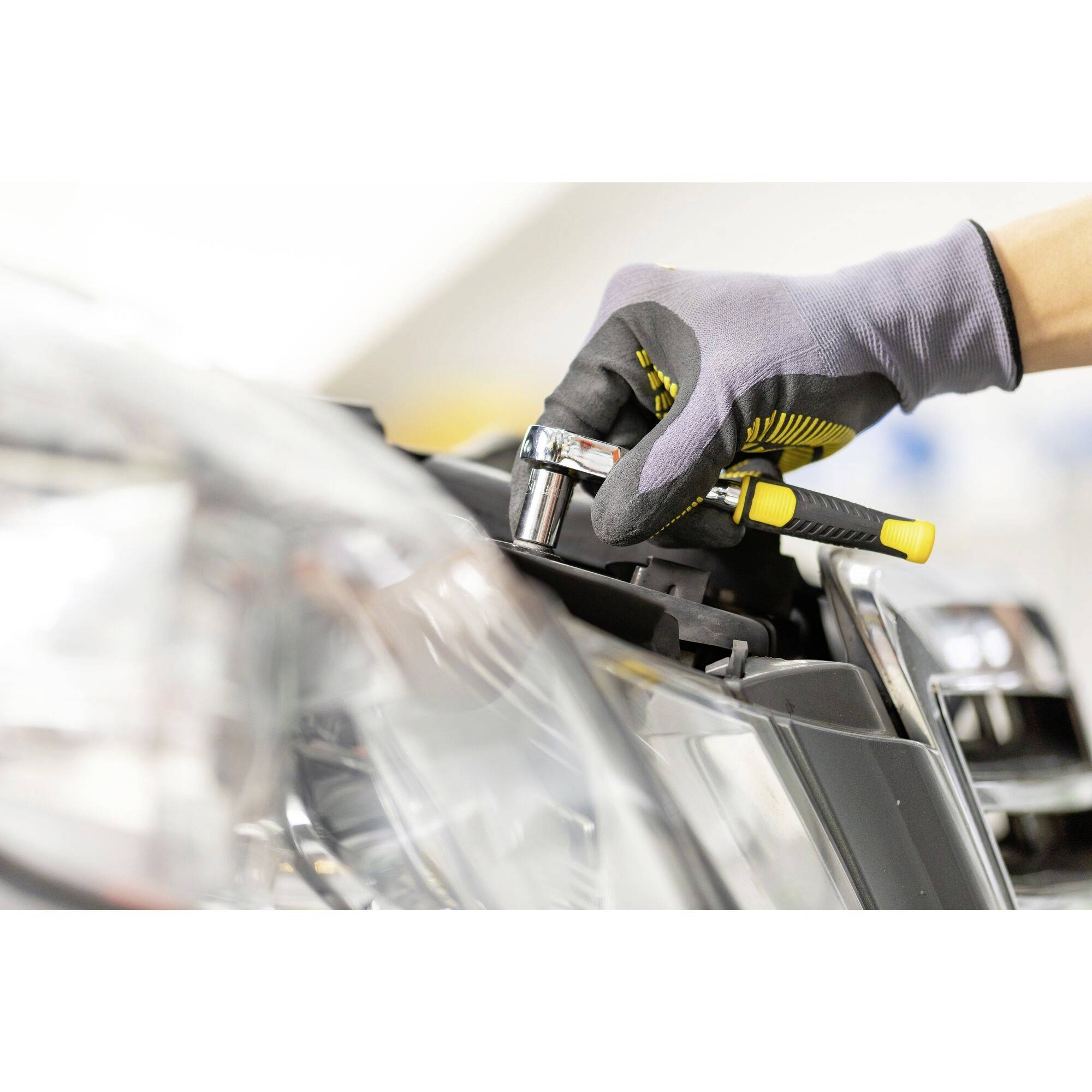 'Eine Person mit Handschuhen verwendet einen Schraubenschlüssel, um eine Schraube an einem Autoteil festzuziehen.'