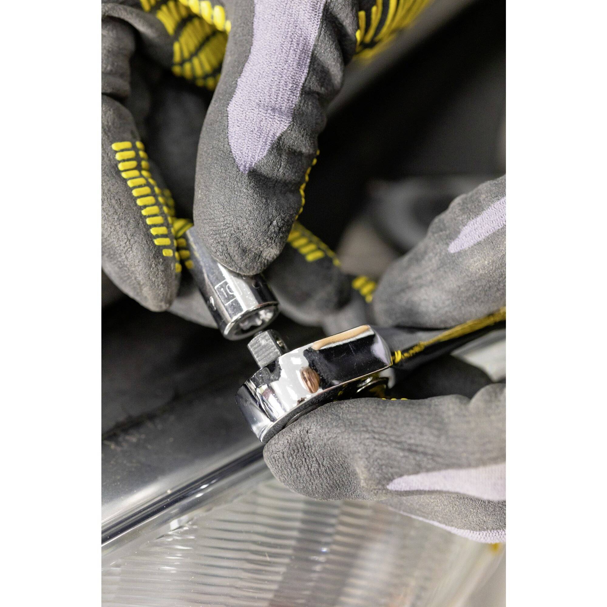 Ein Mechaniker mit grauen Handschuhen arbeitet mit einem Schraubenschlüssel an einer Maschine oder einem Fahrzeug.