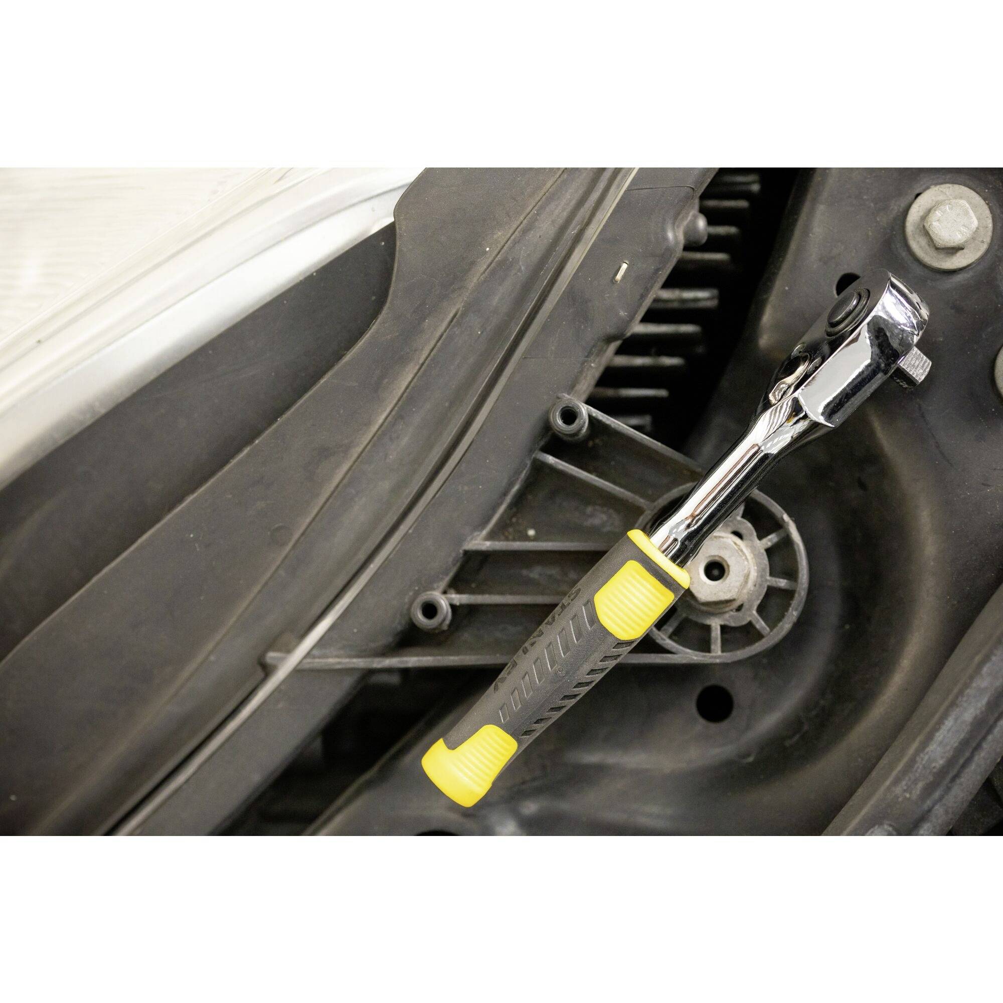 Ein Schraubenschlüssel mit gelbem Griff ist an einer Mechanik, möglicherweise eines Fahrzeugs, angesetzt, um eine Reparatur durchzuführen.