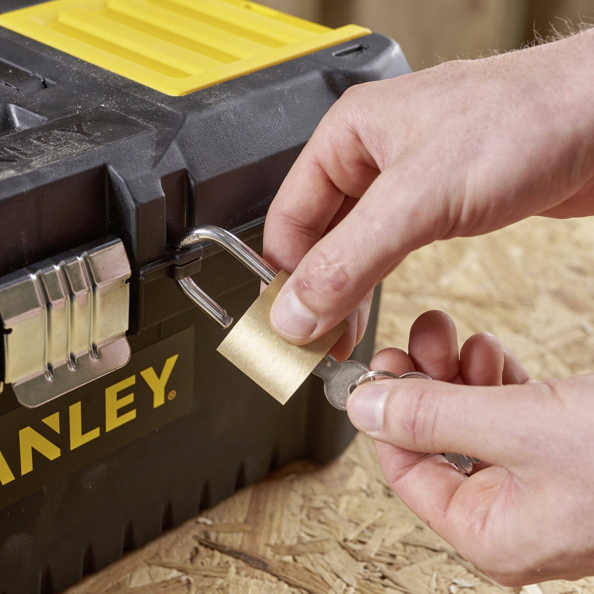 Eine Hand schließt ein kleines Vorhängeschloss an einer schwarzen Werkzeugbox mit einem Schlüssel auf.