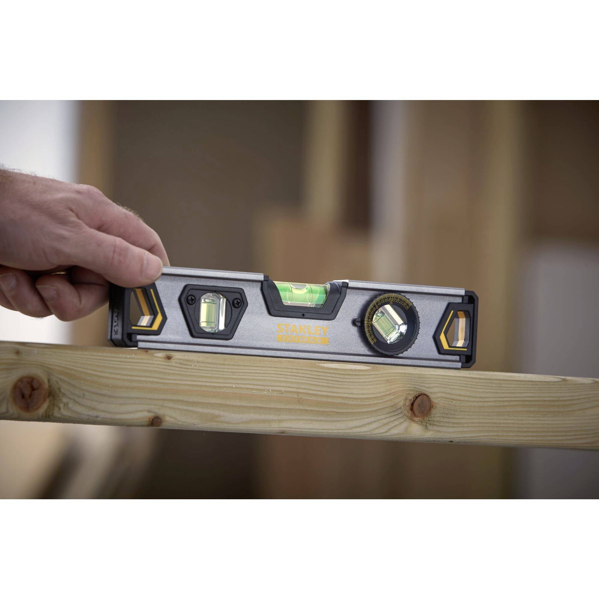 Eine Hand hält eine Wasserwaage auf einem Holzbrett, um die Horizontale zu überprüfen. Die Luftblase befindet sich zwischen den Markierungen.