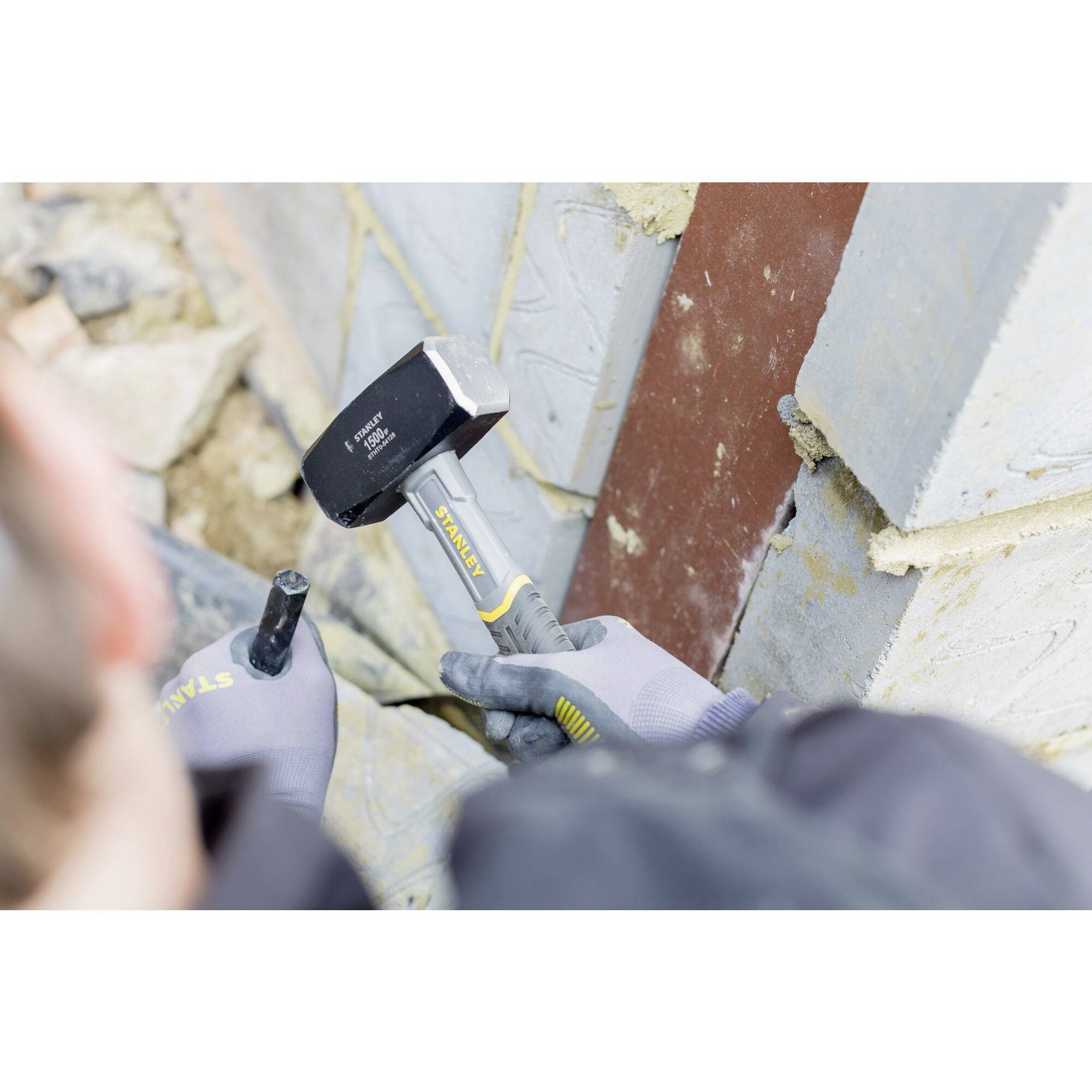 Person mit Handschuhen schlägt mit einem Hammer auf einen Meißel, um Ziegelsteine zu bearbeiten. Renovierungsarbeiten an einer Wand.