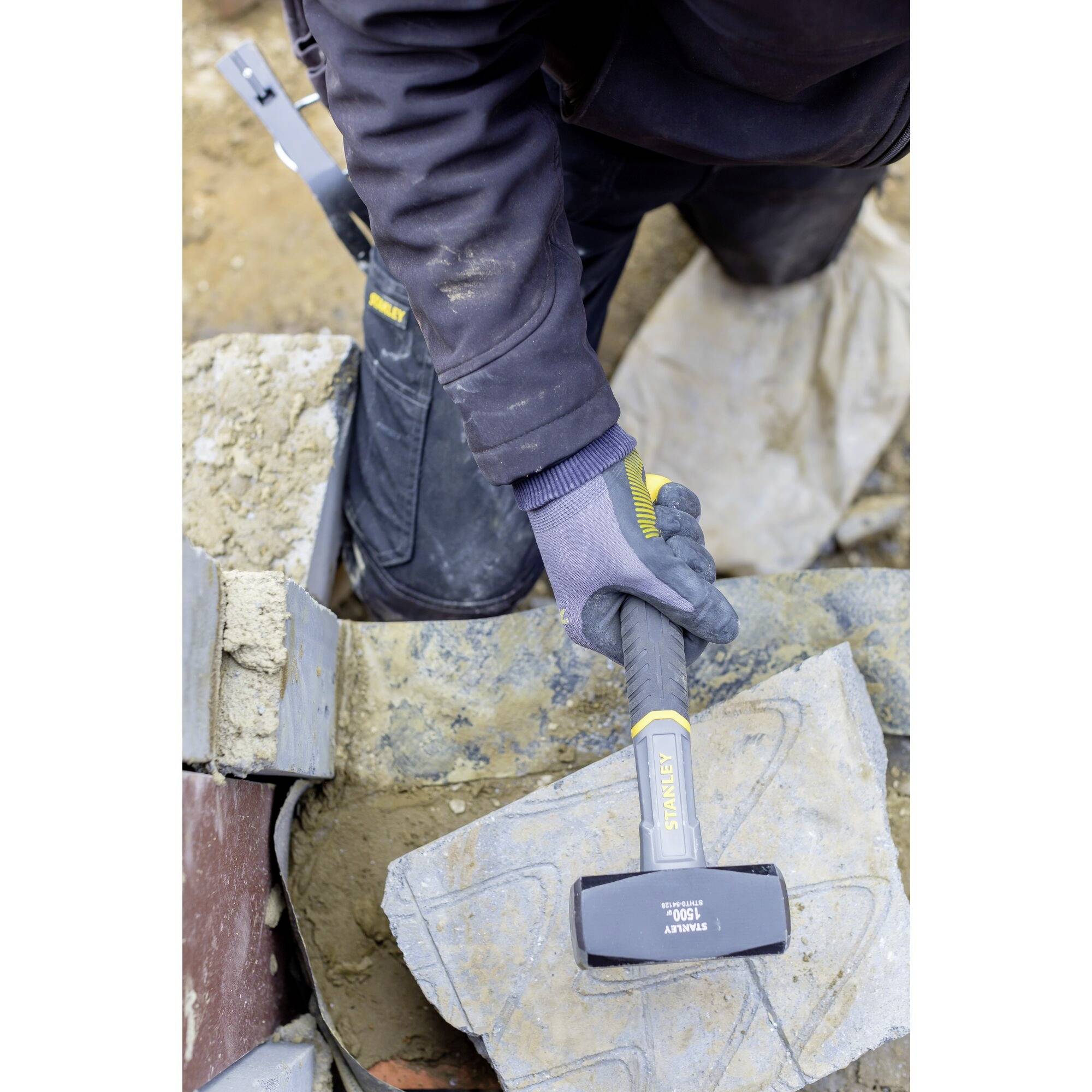 'Arbeiter verwendet Stanley Hammer, um Betonstein auf Baustelle zu bearbeiten. Der Fokus liegt auf dem Werkzeug in Aktion.'