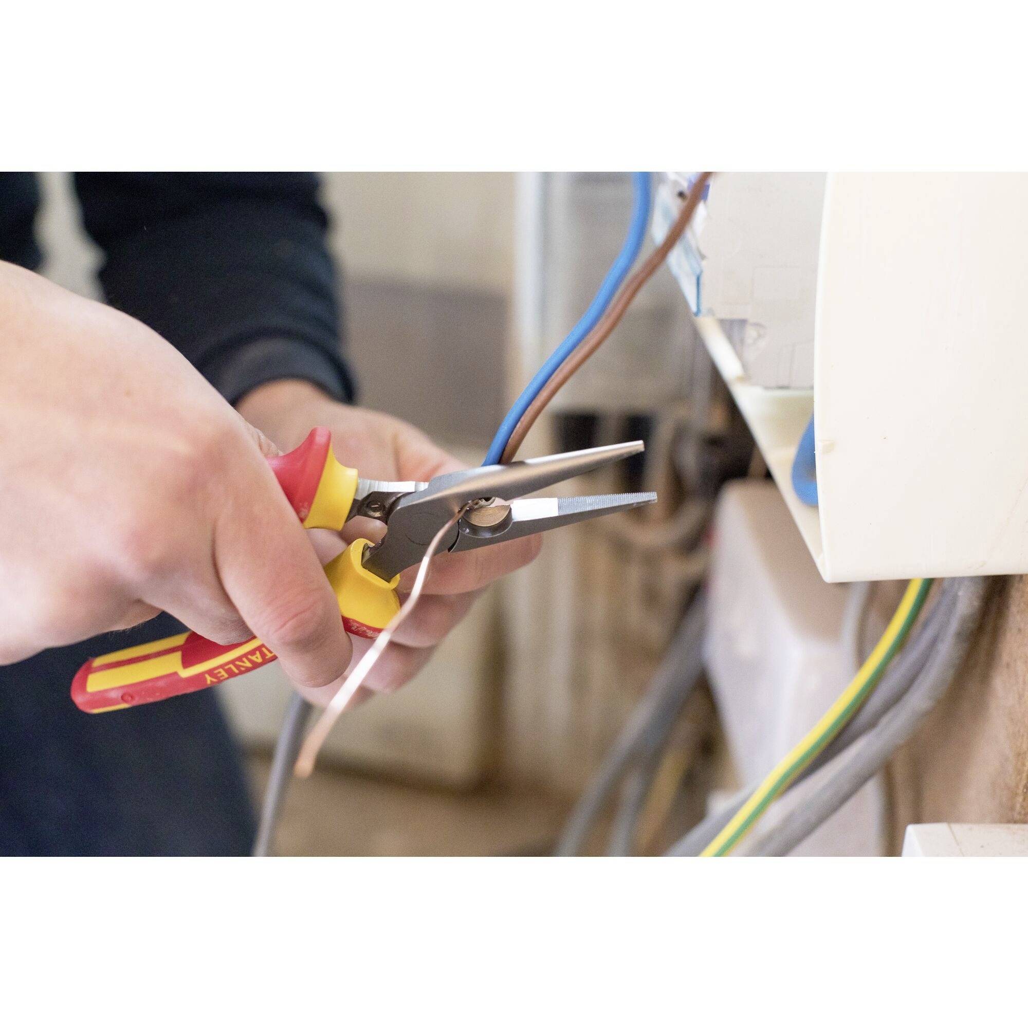 Ein Elektriker schneidet ein Kabel mit einer Zange. Die Szene zeigt präzise Handarbeit an elektrischen Leitungen.