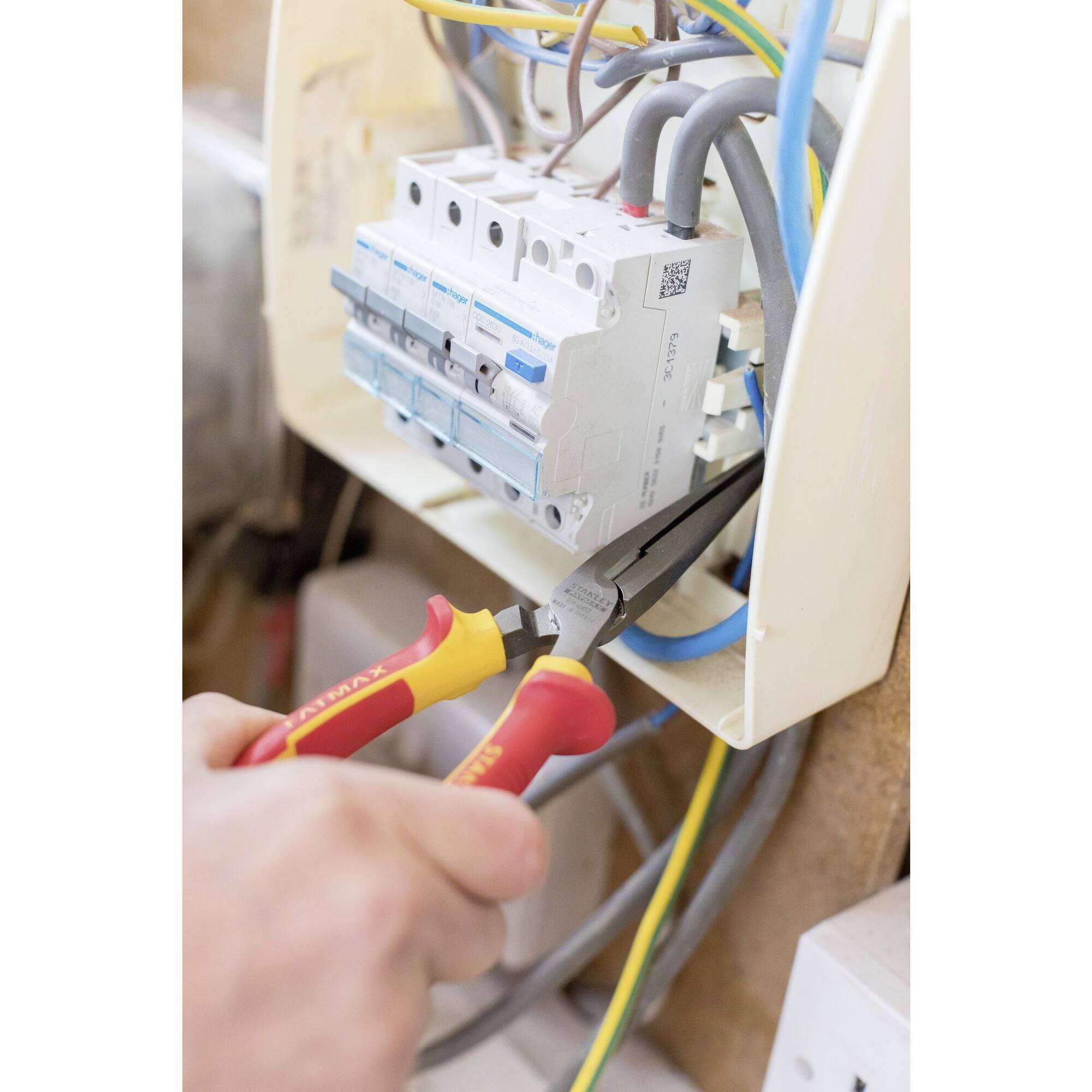 Eine Person benutzt eine Zange, um Drähte in einem elektrischen Sicherungskasten zu bearbeiten. Der Kasten ist offen und zeigt mehrere Drähte.